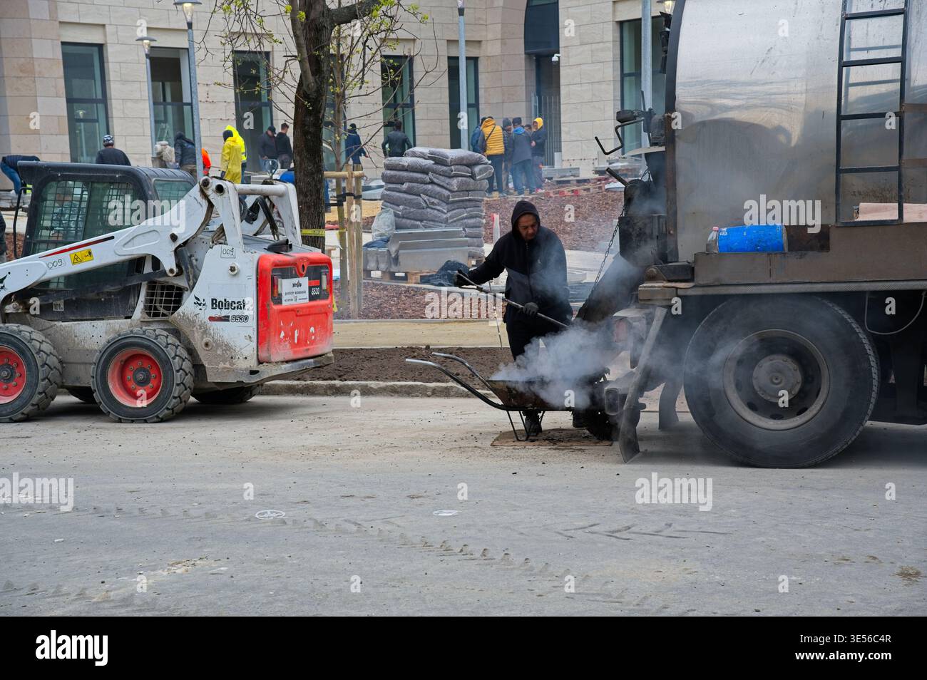 BUDAPEST, UNGHERIA - 28 MARZO 2026: Operai edili e pala Bobcat in un cantiere stradale in asfalto vicino al campus di Ludovika nell'ottavo distretto Foto Stock
