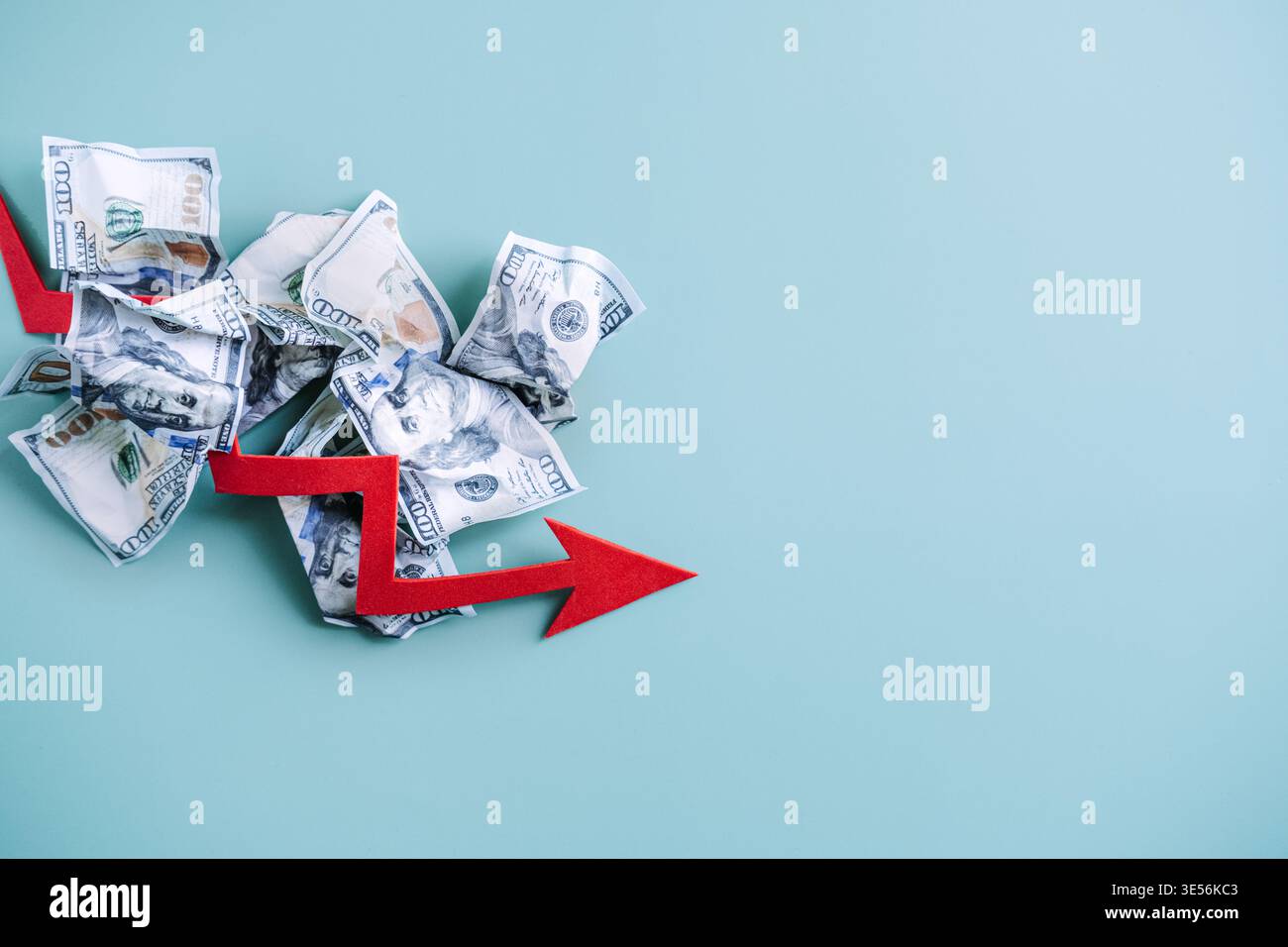 La freccia rossa punta verso il basso sopra la pila di banconote in dollari deformate su sfondo blu. Crescita economica negativa, crisi finanziaria globale, avviso di fallimento Foto Stock