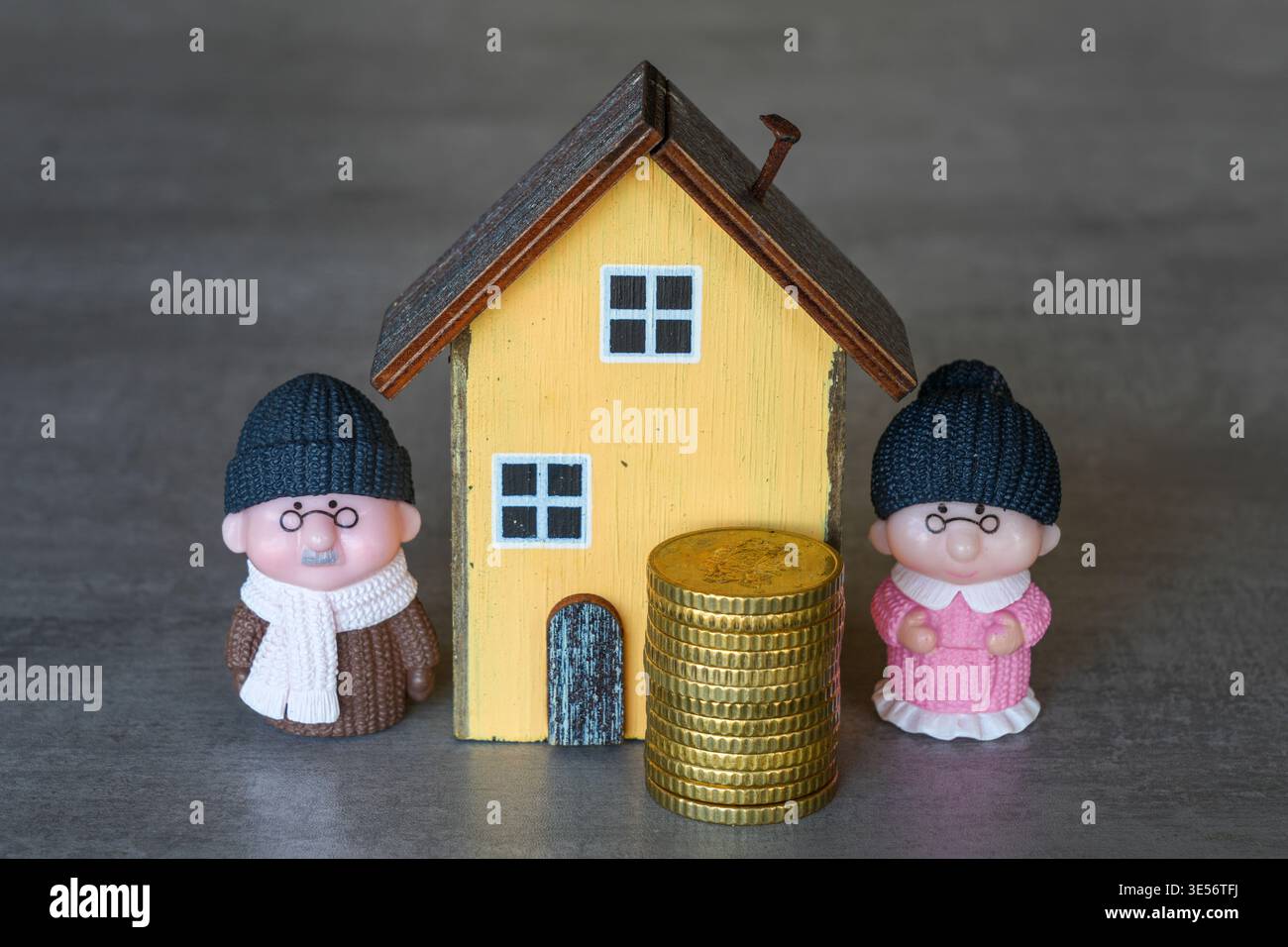 Mini casa con statuette per coppie anziane e pila di monete che simboleggiano la sicurezza dei risparmi pensionistici Foto Stock