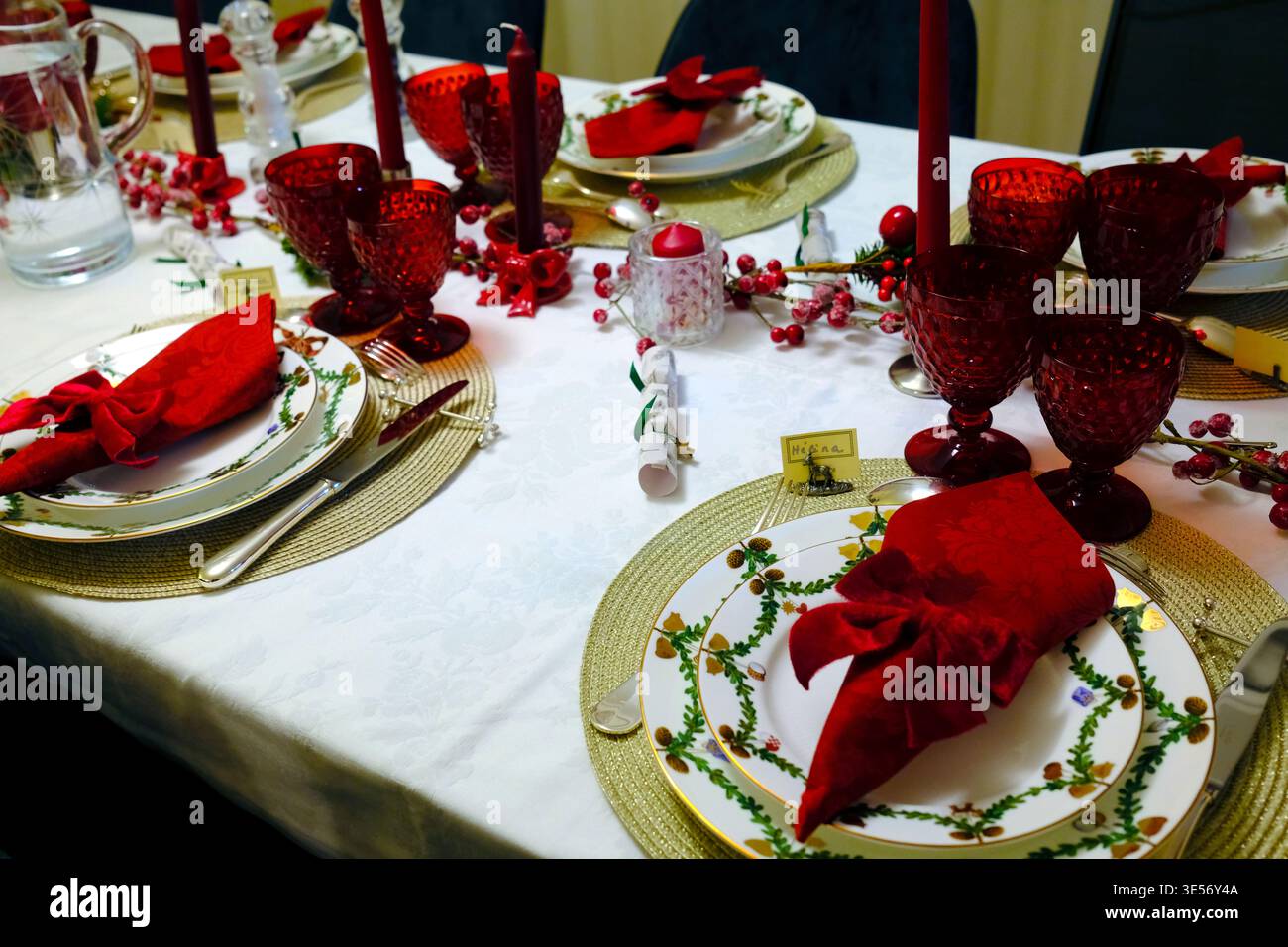Vista sul lungo tavolo natalizio con bicchieri rossi, candele alte e ambienti eleganti. Foto Stock