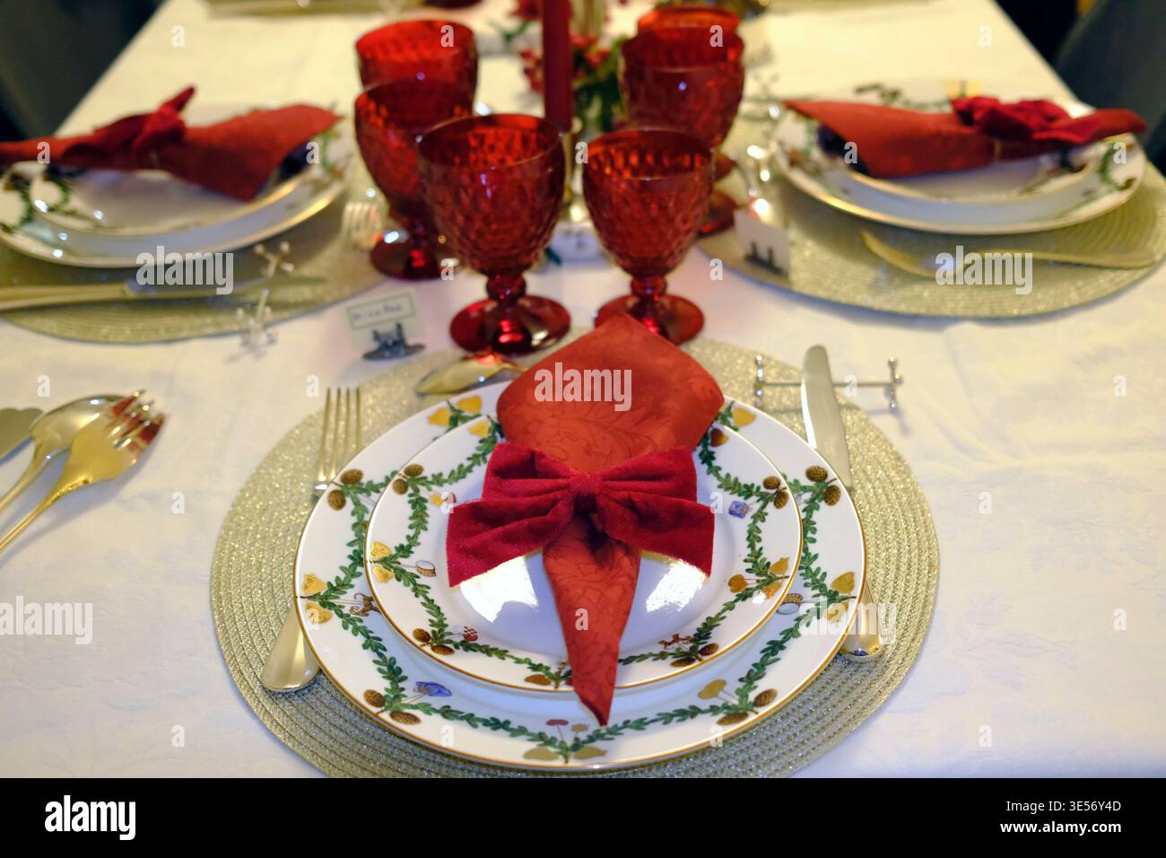 Vista sul lungo tavolo natalizio con bicchieri rossi, candele alte e ambienti eleganti. Foto Stock