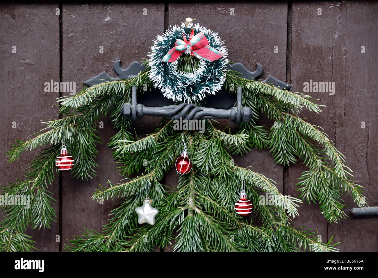 Elegante corona naturale di Natale fatta di coni di pino, frutti di bosco e rami di abete appesi su una porta di legno. Saint Gervais. Francia. Foto Stock