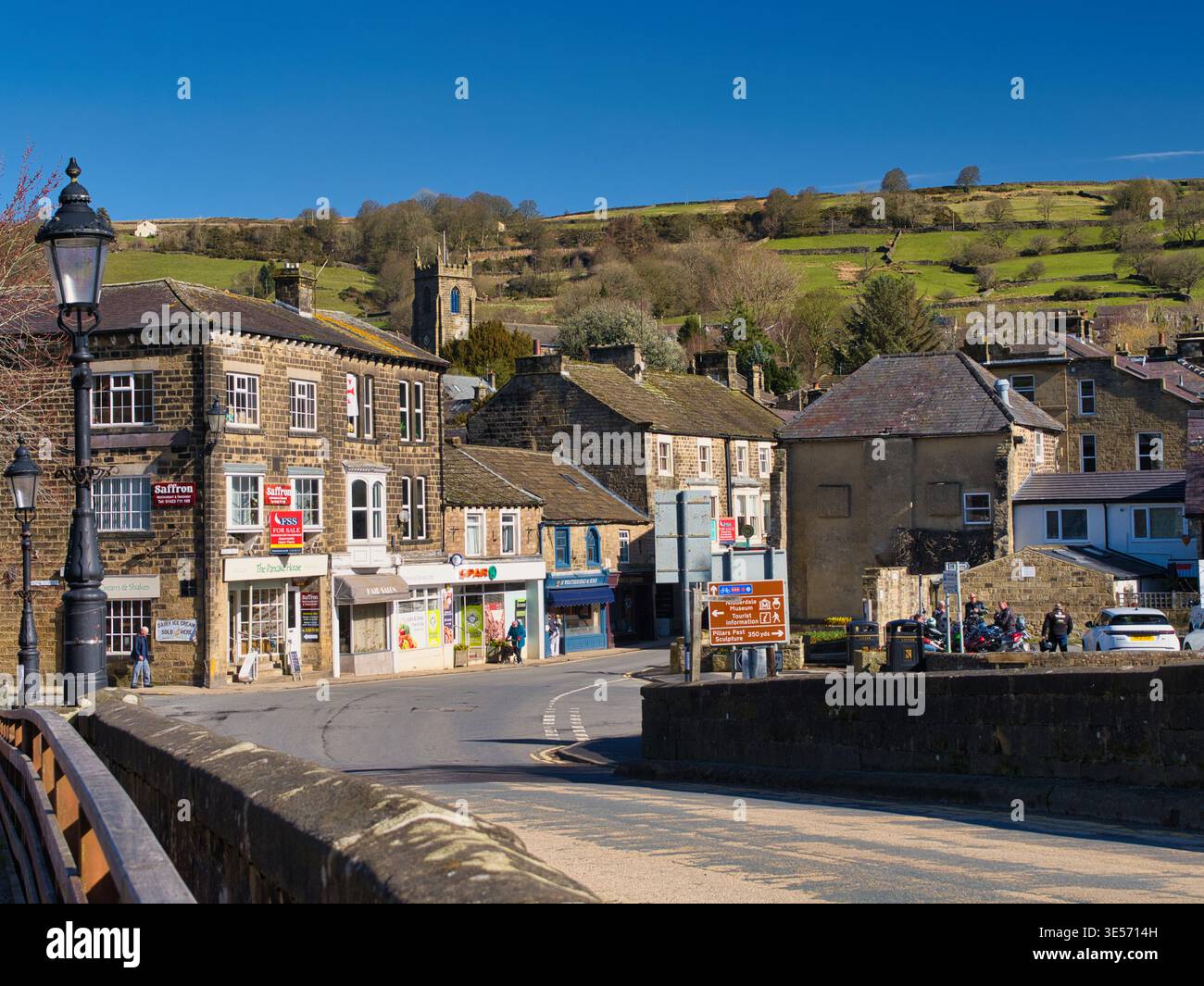 Yorkshire, UK - 17 mar 2026: Vista soleggiata di Pateley Bridge nello Yorkshire UK con edifici in pietra, negozi di paese e sfondo di colline verdi sotto un cielo blu brillante Foto Stock