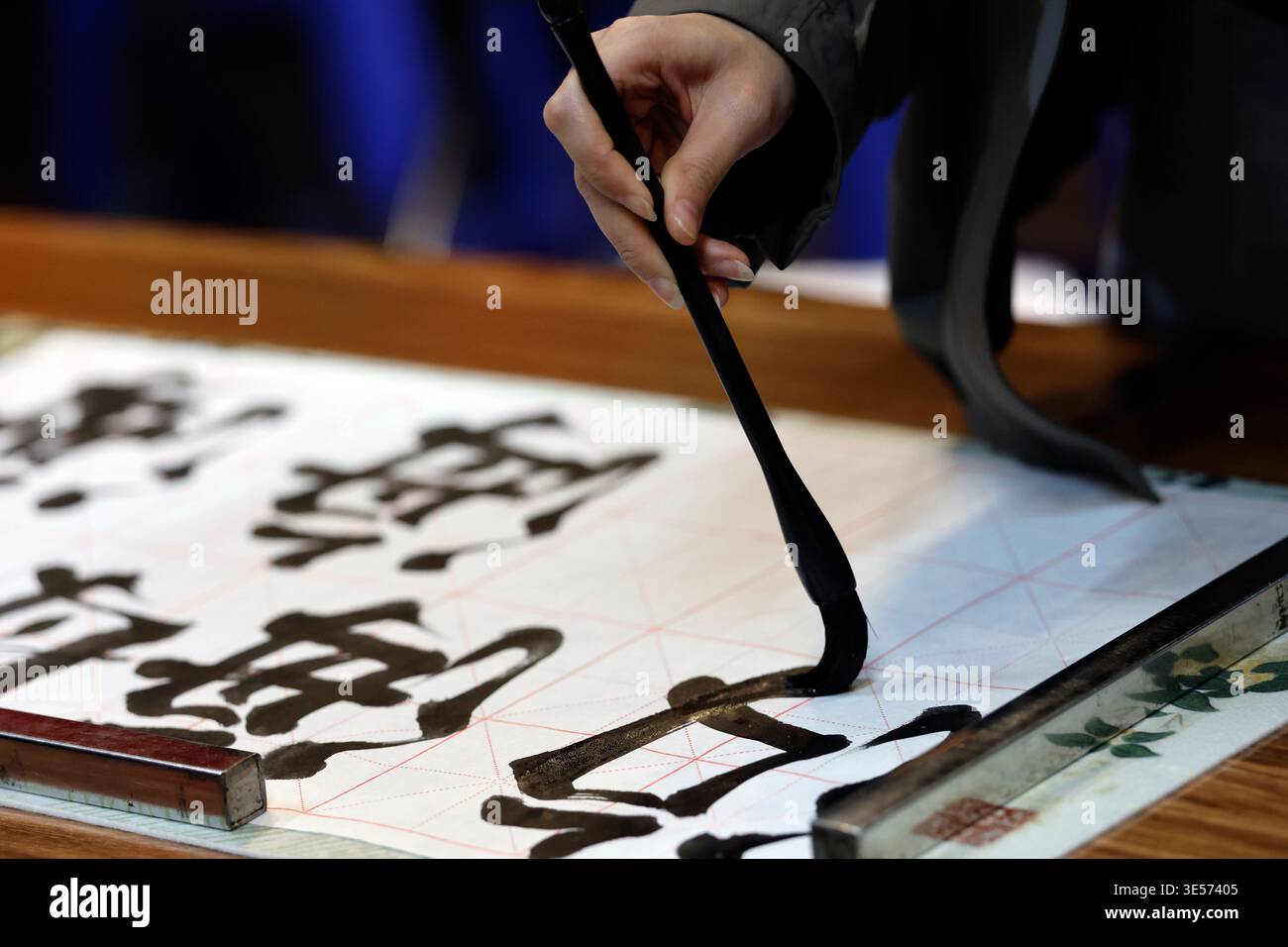 Primo piano di una mano che regge un pennello calligrafico con caratteri cinesi audaci su carta a griglia. Hanoi. Vietnam. Foto Stock