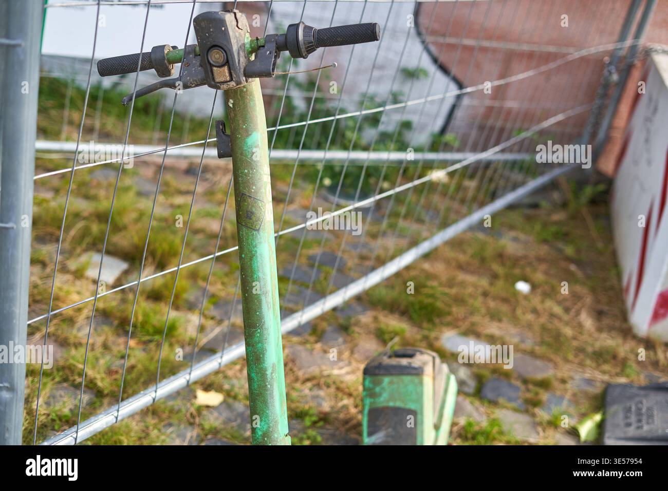Vista ravvicinata del manubrio verde di uno scooter con impugnature in gomma nera, posizionato di fronte a una recinzione metallica. Lo scooter Foto Stock