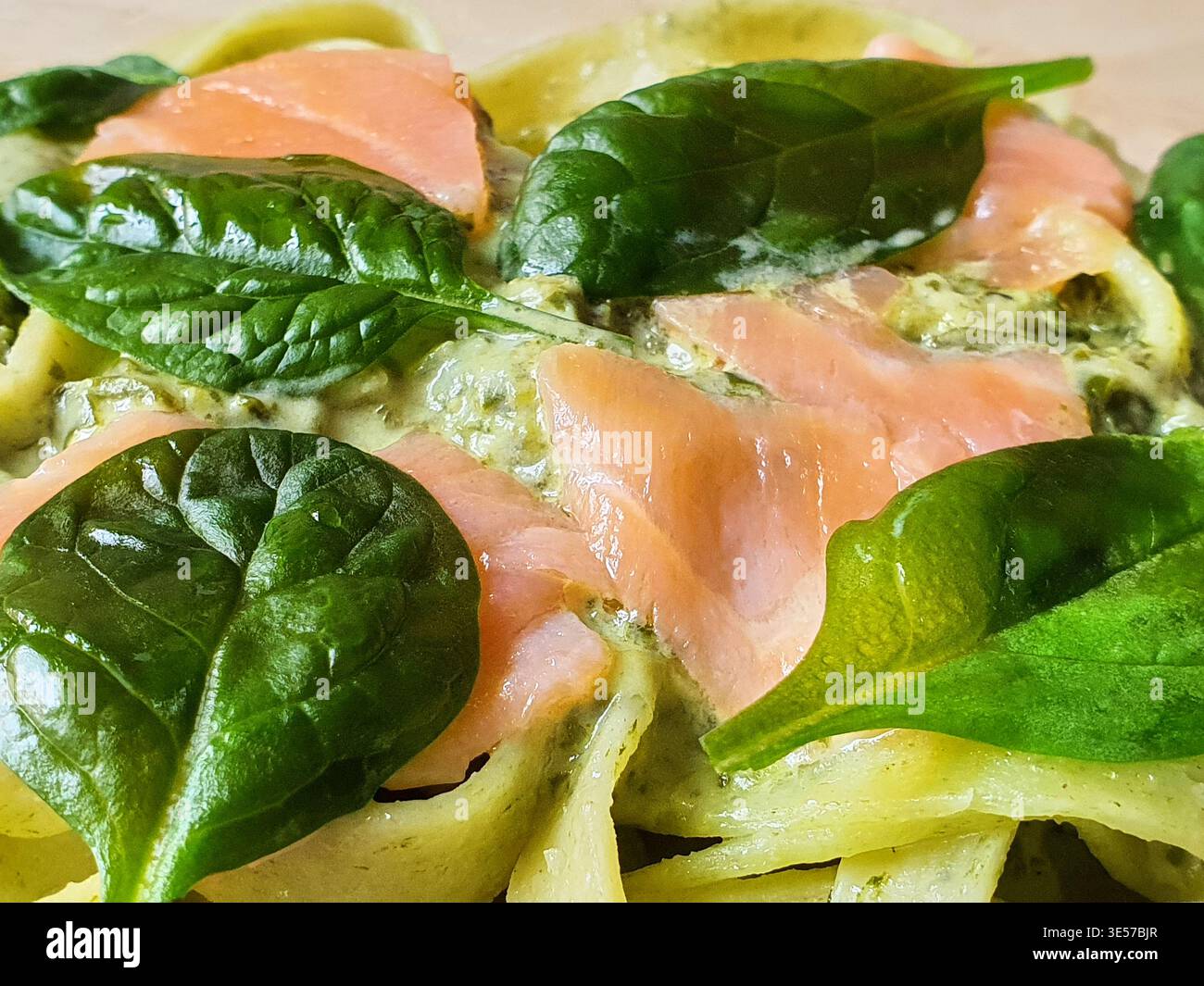 Una foto macro di primo piano di un piatto di pasta italiana con ampi tagliatelle a nastro ricoperte da una cremosa salsa verde, ricoperta da fette di rosa affumicato Foto Stock