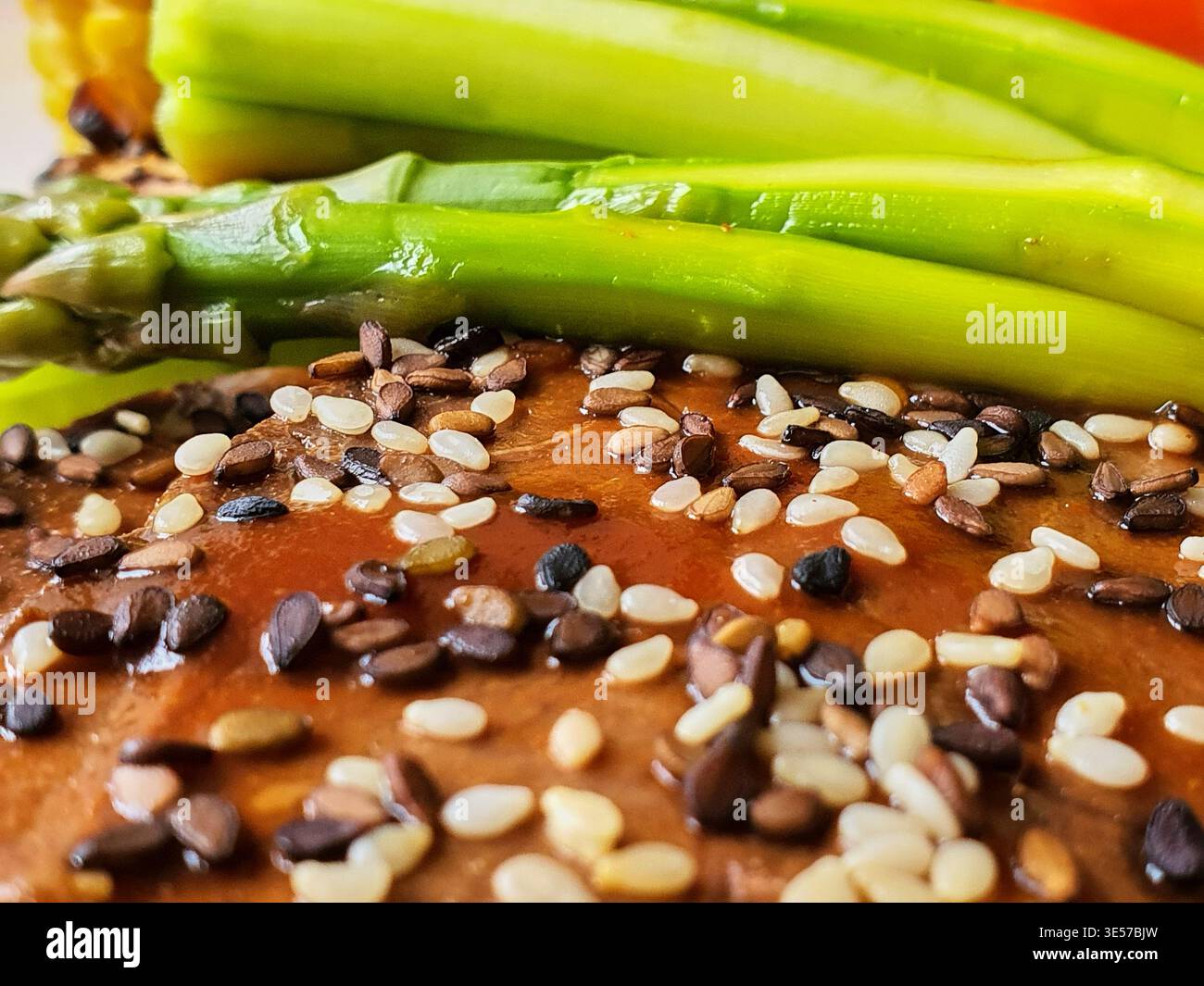 Fotografia macro di cibo in primo piano con lancette di asparagi verdi fresche appoggiate su una salsa o condimento marrone lucido, abbondantemente condite con un misto Foto Stock
