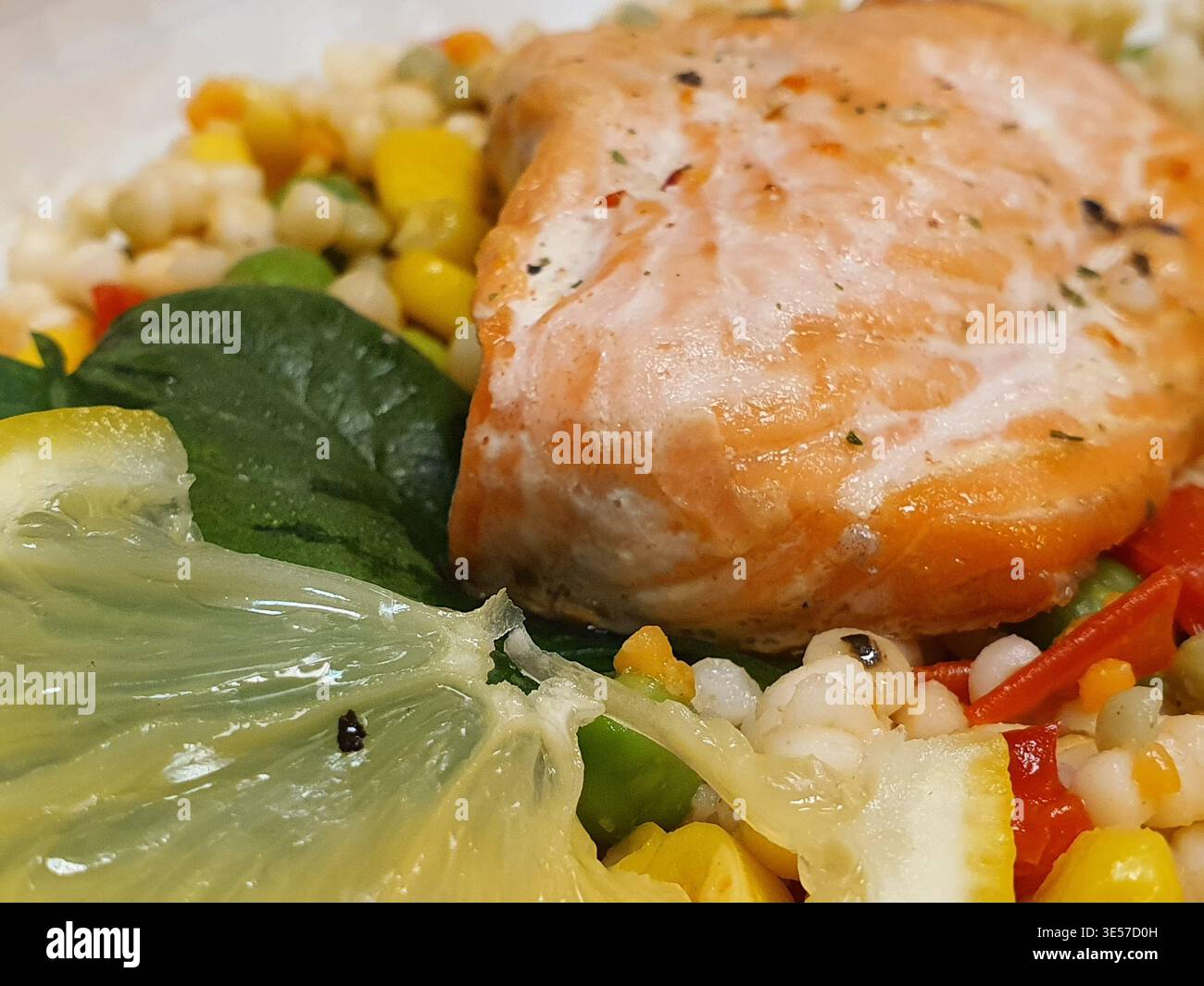 Foto ravvicinata di un filetto di salmone cotto appoggiato su un letto colorato di verdure e cereali misti. Il salmone presenta una tonalità rosa-arancio Foto Stock