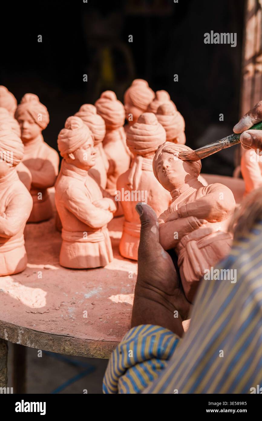 Un abile artigiano aggiunge dettagli intricati alle statuette in argilla in un vivace mercato indiano. Le mani danno vita a ogni pezzo, mettendo in risalto l'artigianato tradizionale Foto Stock