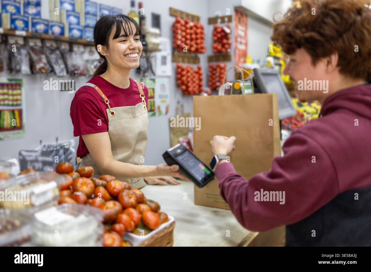 Un allegro assistente di un negozio di frutta aiuta un cliente con l'acquisto al banco cassa. Il negozio propone prodotti freschi, enfatizzando Foto Stock