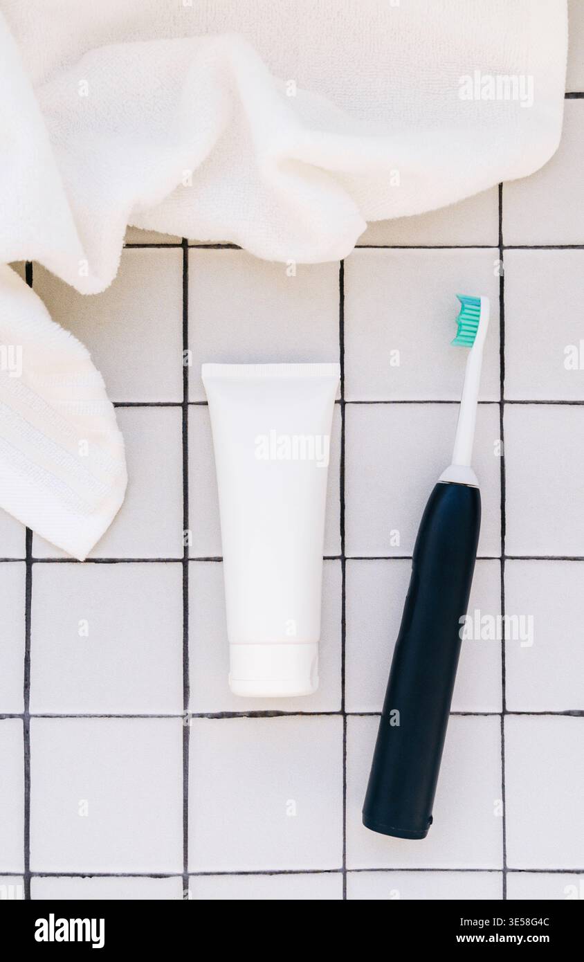 Spazzolino da denti e dentifricio con contenitore bianco su fondo piastrellato, concetto minimo di igiene del bagno, composizione piatta. Vista dall'alto Foto Stock