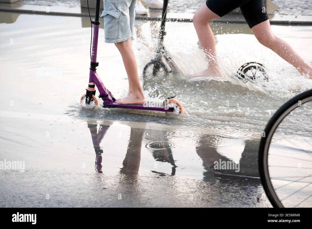 Due bambini che attraversano acque poco profonde con scooter e riflessi a specchio Foto Stock