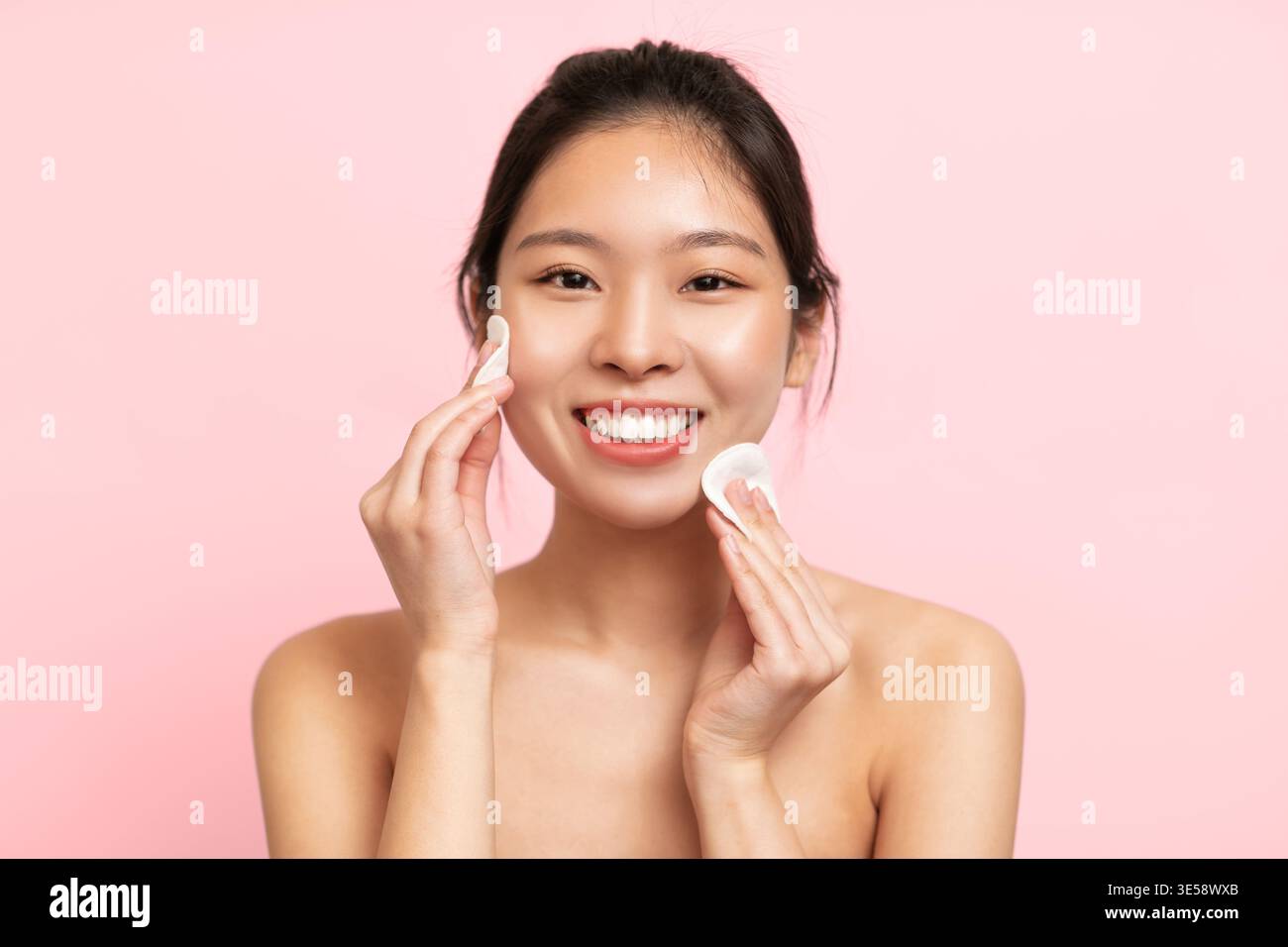 Donna che applica la Skincare sul suo viso contro uno sfondo rosa in una routine di bellezza Foto Stock