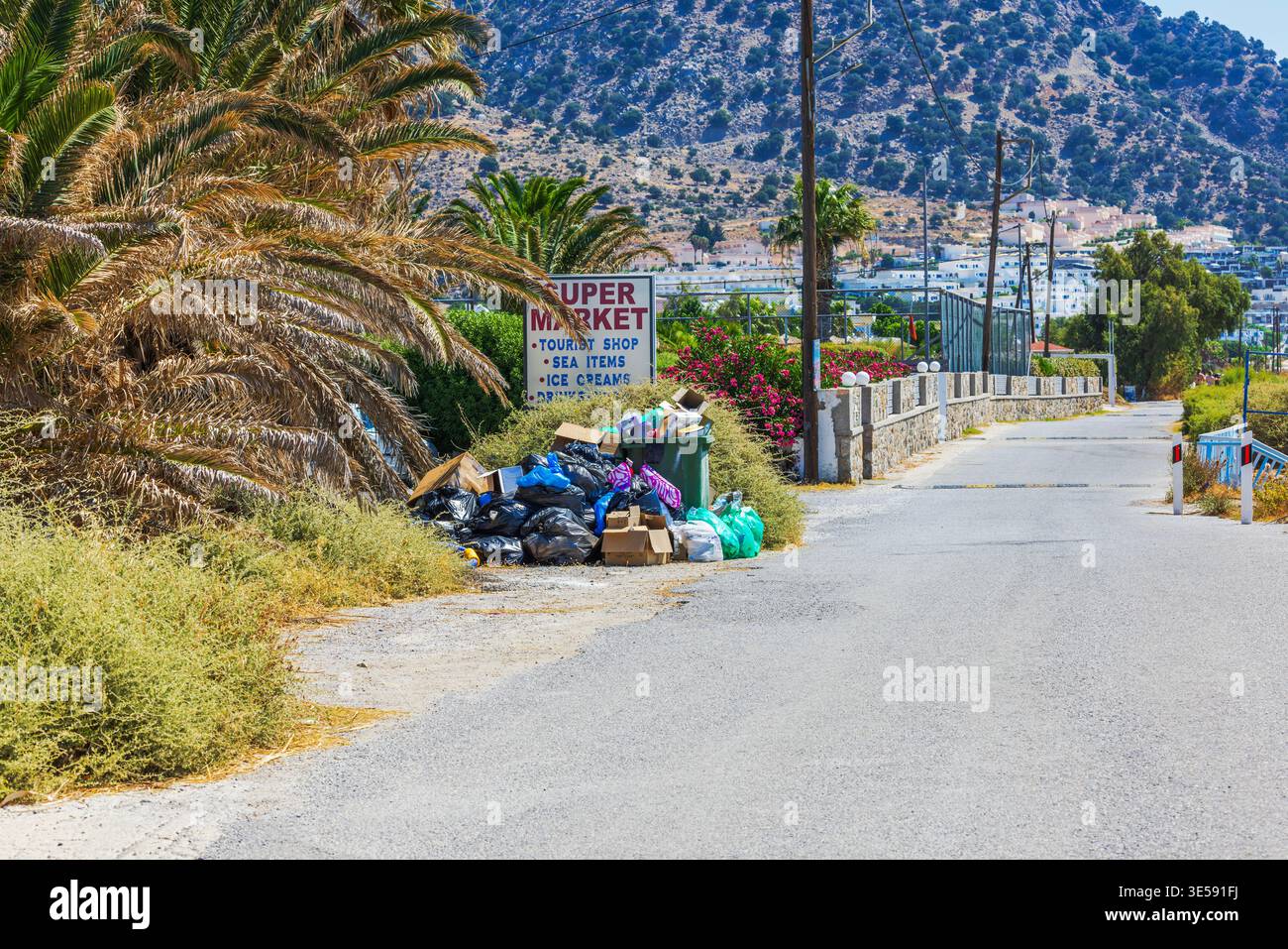 Vista ravvicinata della strada costiera con pali di spazzatura vicino alla spiaggia con il Mar Egeo e le montagne. Kos. Grecia. Foto Stock