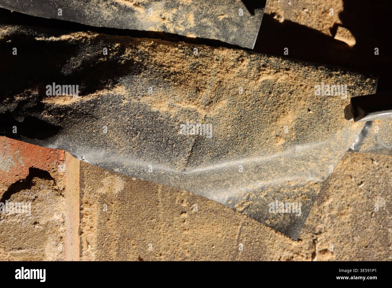 La luce del sole della sera illumina un contrasto di texture tra i materiali da costruzione e l'accumulo di polvere su un tavolo in mattoni. Foto Stock