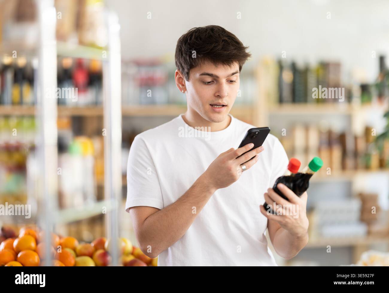 L'acquirente maschio verifica l'idoneità - scansiona il codice QR sull'etichetta della salsa di soia nel negozio di alimentari Foto Stock