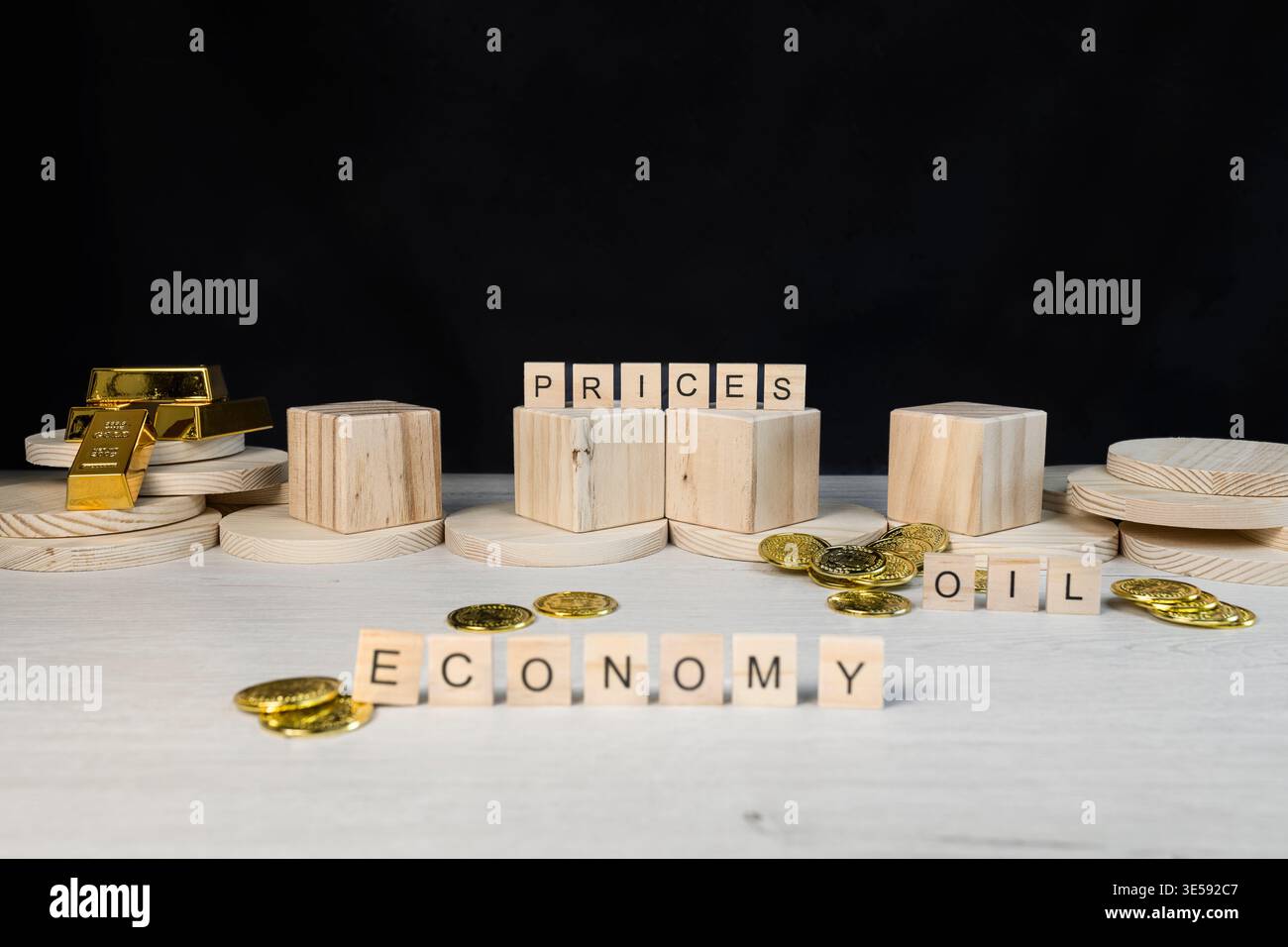Economia scritta in blocchi di legno che mostrano i prezzi dei lingotti d'oro e del petrolio con monete, visualizzando l'impatto delle fluttuazioni del mercato e della finanza globale st Foto Stock