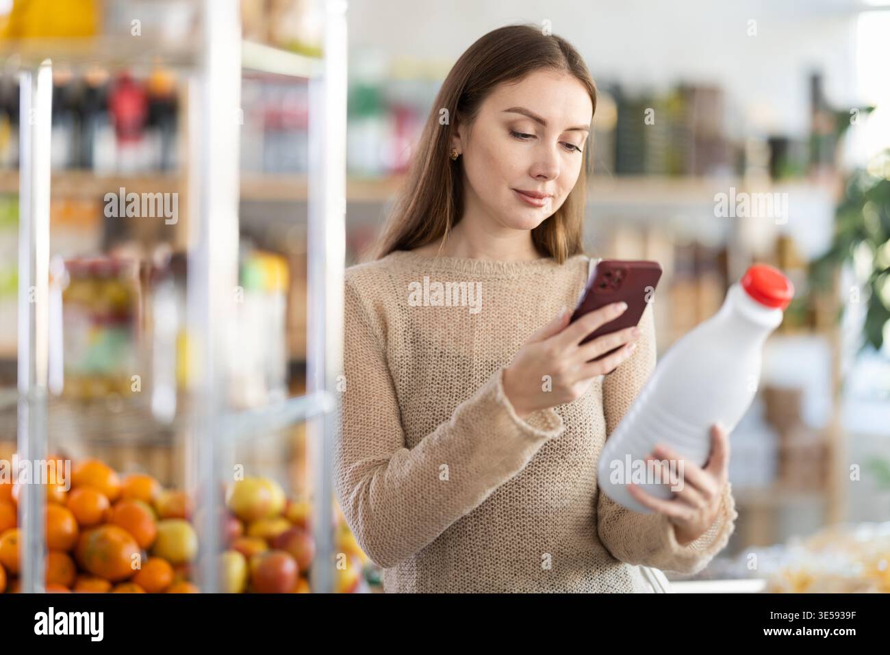 L'acquirente donna esegue la scansione del codice QR sull'etichetta del latte nel negozio di alimentari Foto Stock