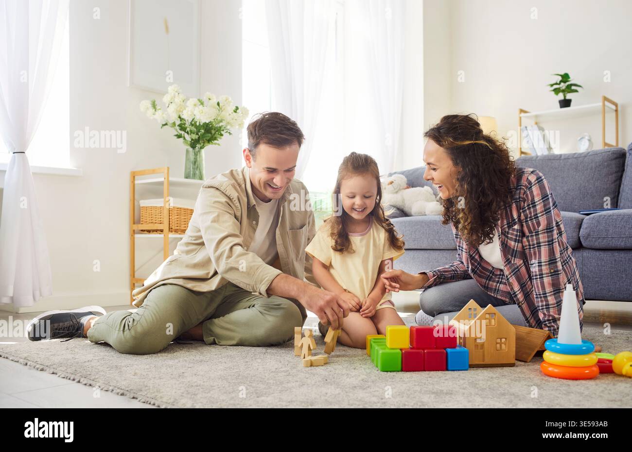 Genitori felici e figlia che giocano con giocattoli di legno in un luminoso soggiorno Foto Stock