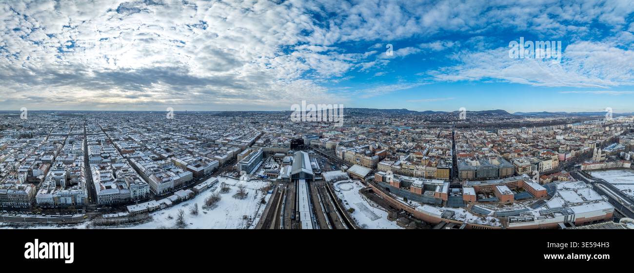 Ampia vista panoramica dalla stazione ferroviaria di Nyugati, tetti innevati, Parlamento a sinistra, ponti sul Danubio, colline di Buda, cielo blu Foto Stock