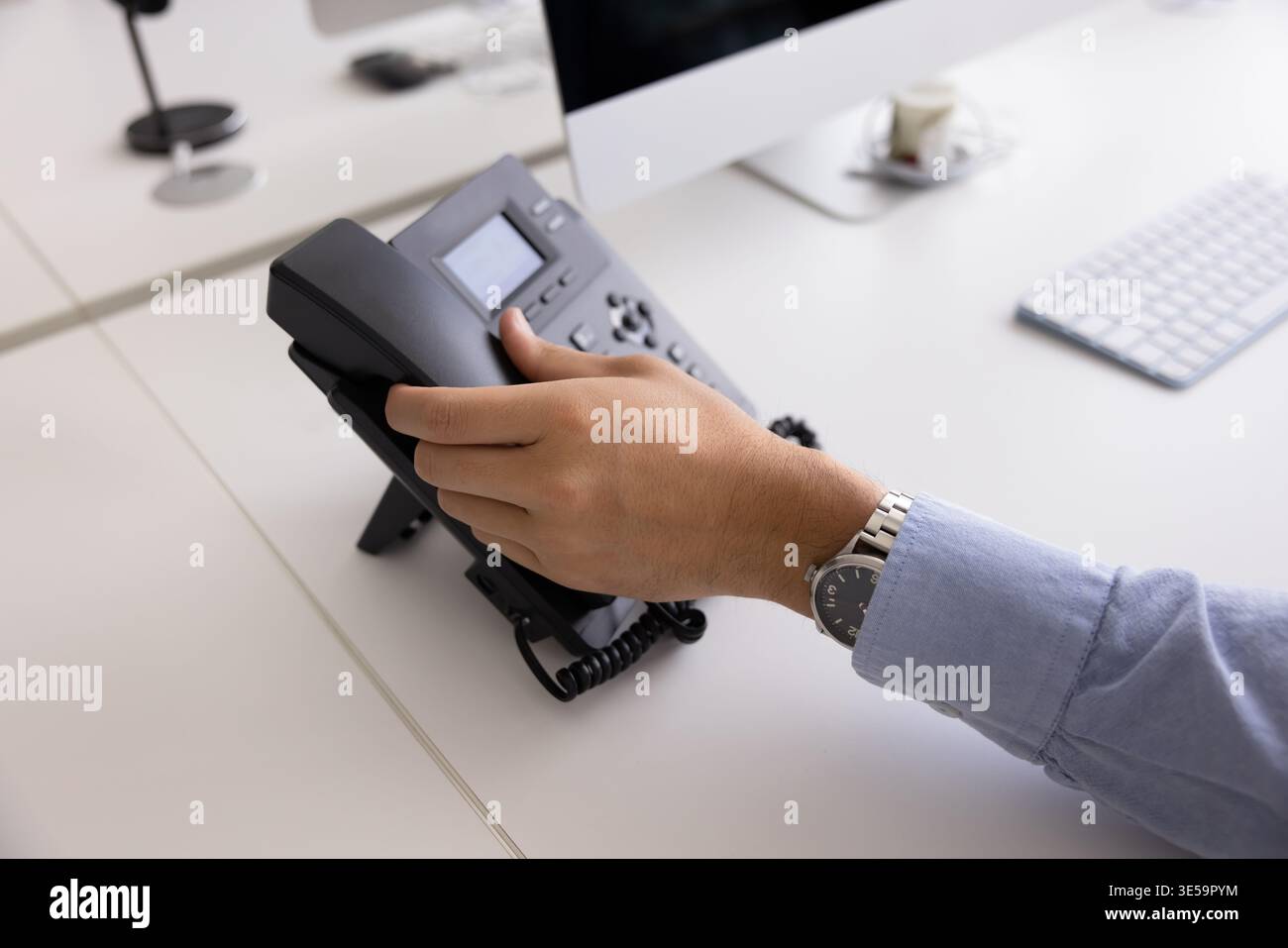 Un uomo d'affari può portare a mano il ricevitore del telefono fisso sulla scrivania Foto Stock