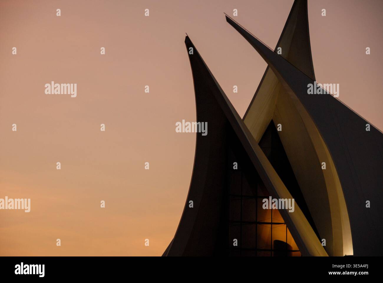 Guglie geometriche affilate perforano un caldo cielo turchese al tramonto in questa fotografia architettonica moderna. Le forme angolari di grande impatto creano silhouette accattivanti Foto Stock