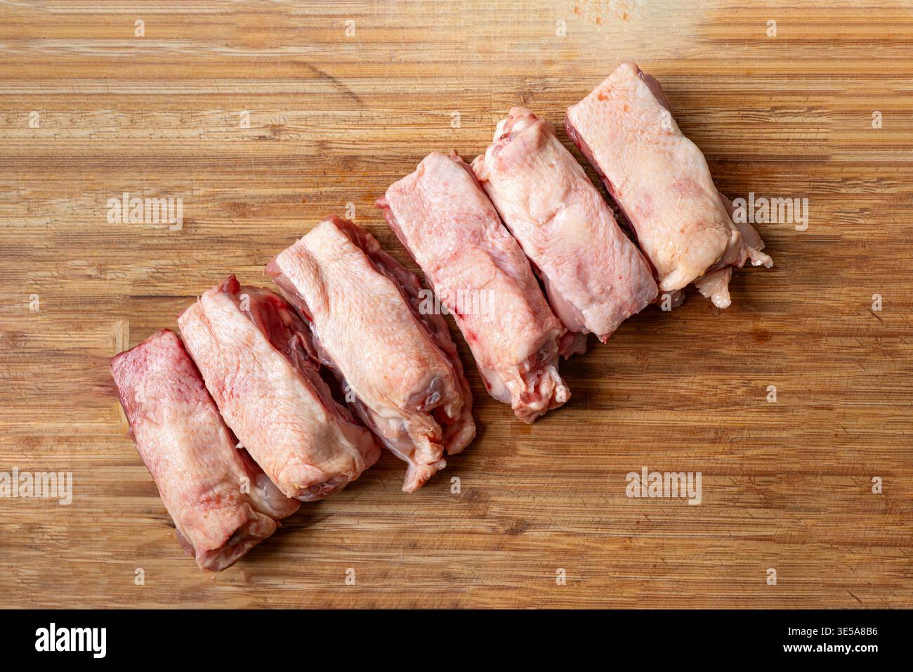 Una fila di dorsi di pollo crudi freschi tagliati a pezzi su un tagliere di legno. Primo piano, niente gente Foto Stock