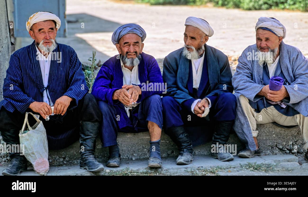 Quattro vecchi si riuniscono in una strada a Samarcanda. Indossano abiti tradizionali e condividono storie alla luce del sole. Foto Stock