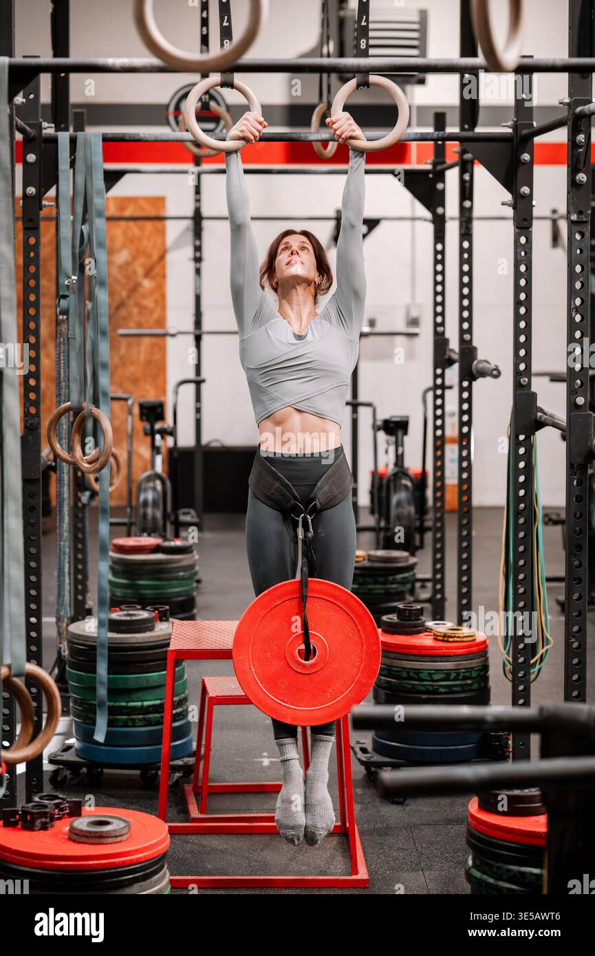 Donna che esegue un esercizio sospeso con una piastra per pesi in palestra Foto Stock