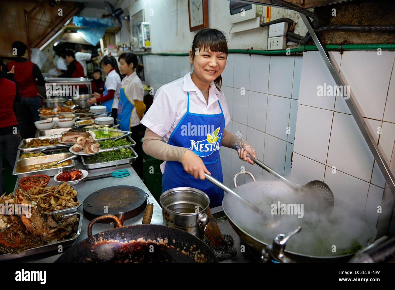 Gli chef preparano piatti mentre lavorano in una cucina affollata ad Hanoi. La scena mostra il cibo cucinato e servito ai clienti. Foto Stock
