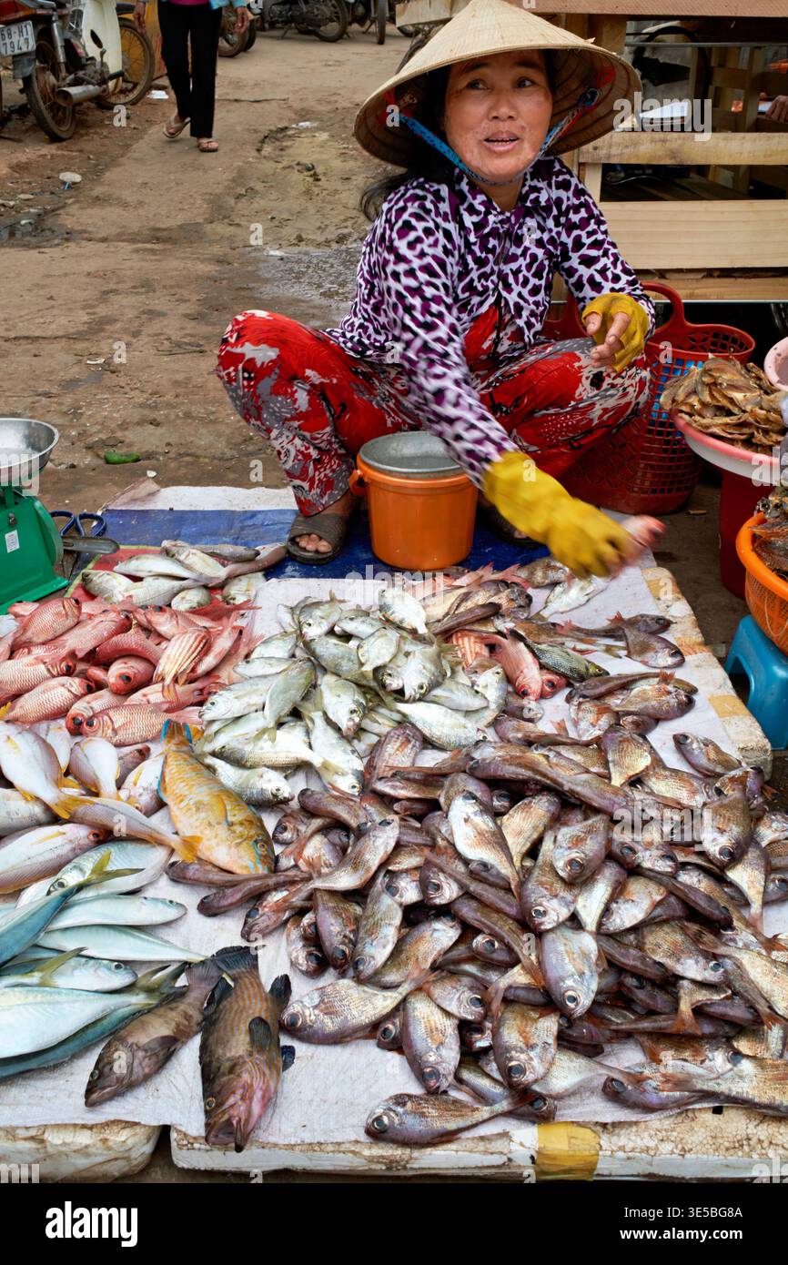 Un venditore siede in un mercato a Phu Quoc, Vietnam. Mostra vari pesci per i clienti. La gente passeggia ed esplora la zona. Foto Stock