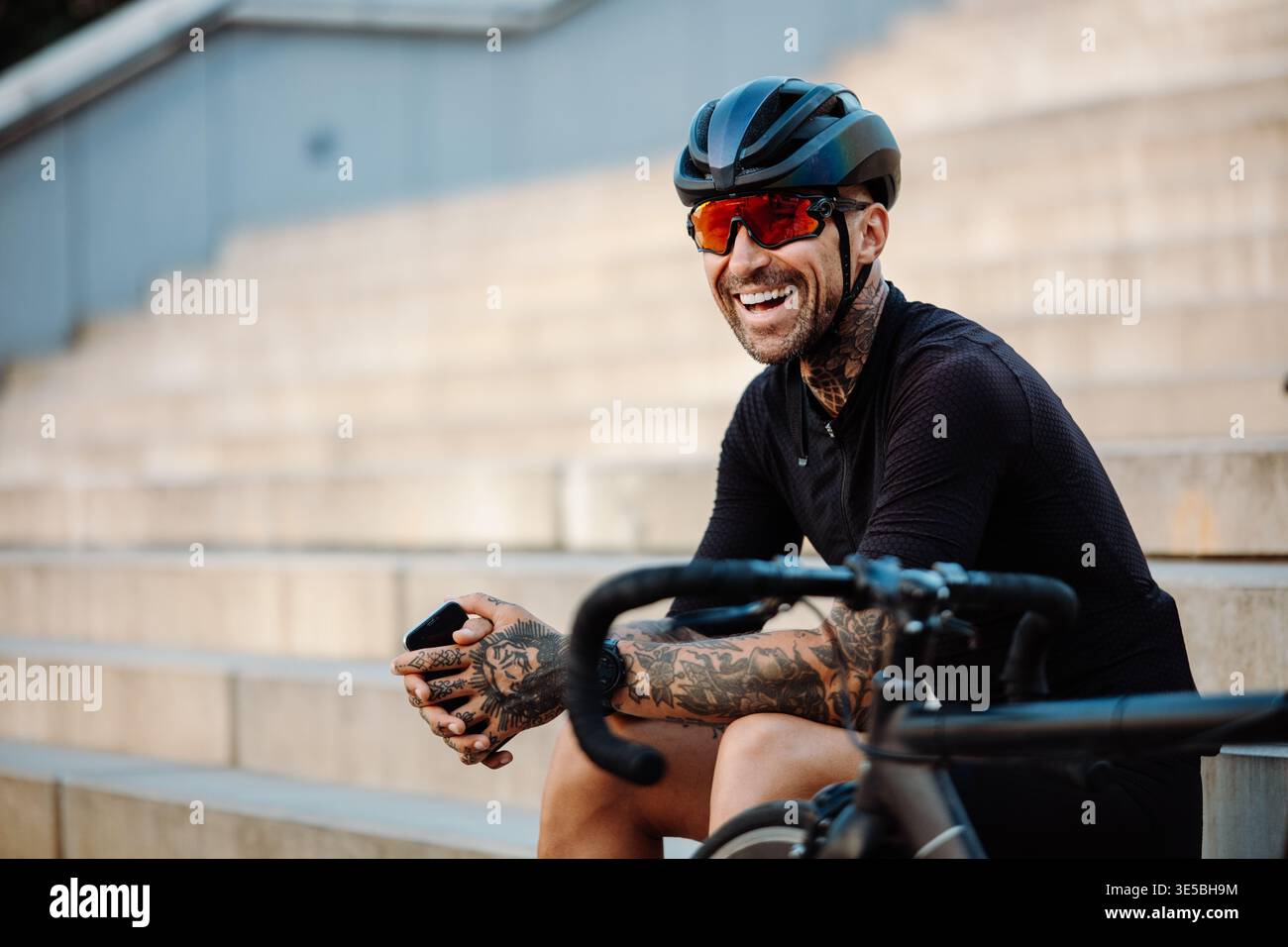 Urban male ciclista sorridente e rilassante dopo il giro con equipaggiamento visibile e attitudine sicura Foto Stock