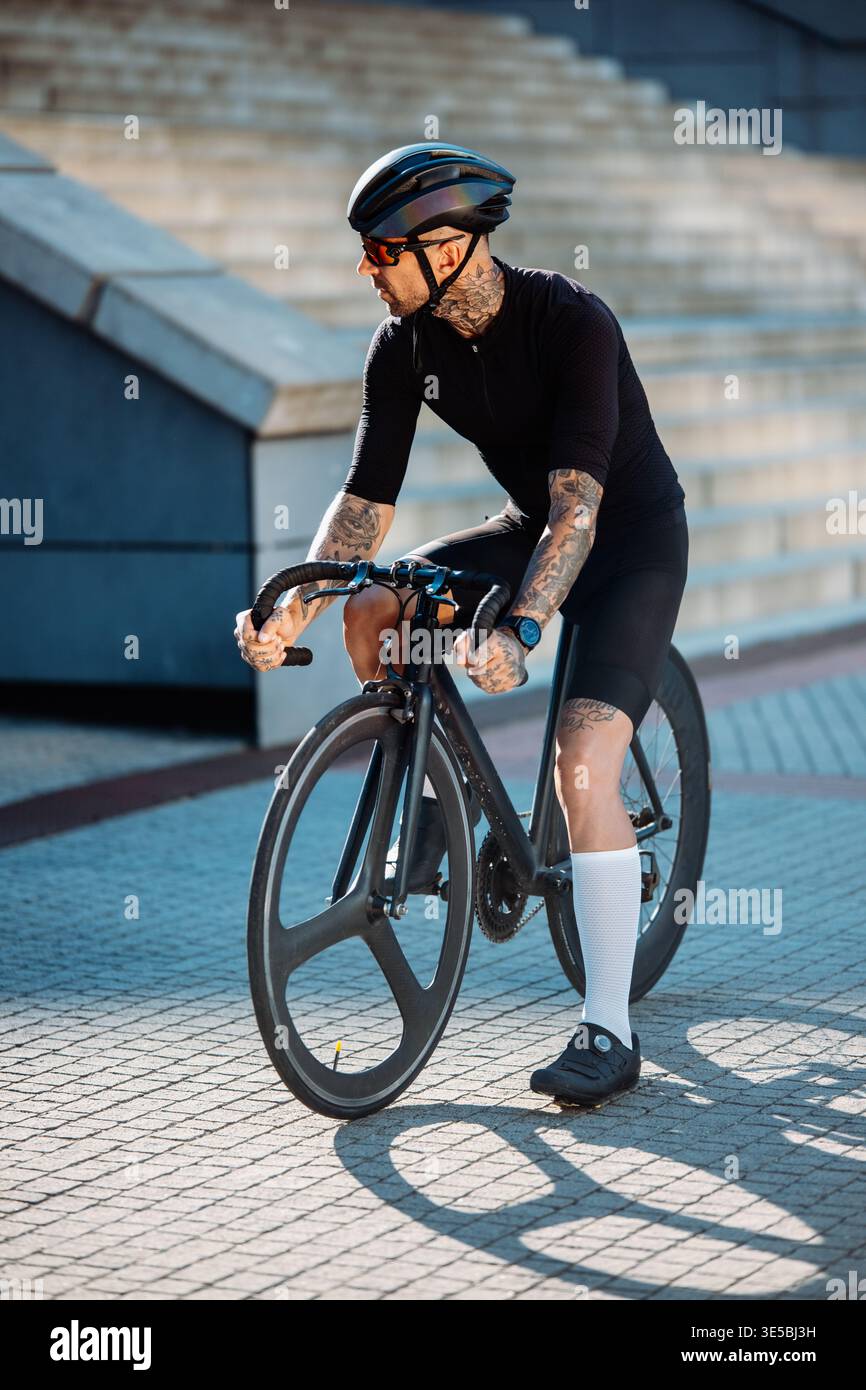 Abile ciclista maschile con occhiali riflettenti che si gode di un tranquillo viaggio urbano sotto la calda luce del sole Foto Stock