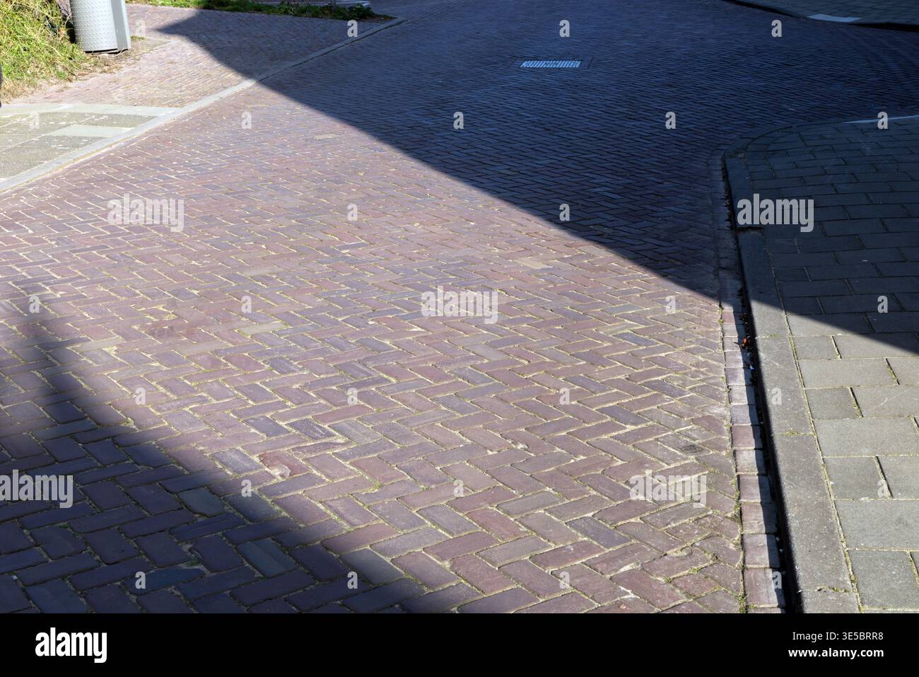 Luce solare e ombra creano un contrasto geometrico su una superficie in mattoni lastricati in un ambiente urbano all'aperto. Foto Stock