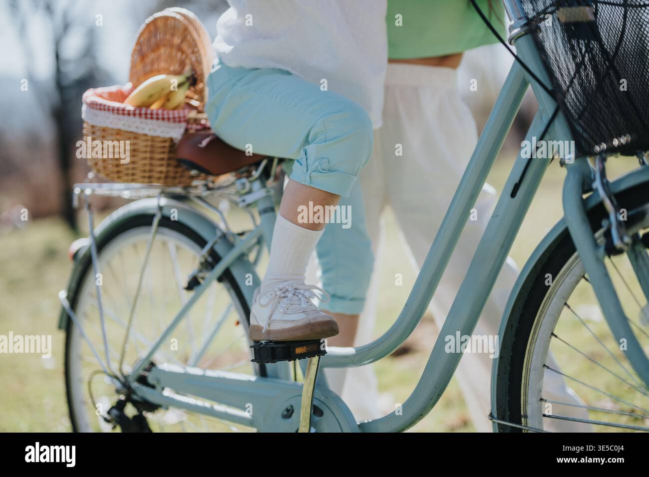 Mamma insegna alla figlia a fare un giro in bicicletta vintage con un cestino da picnic nel parco Foto Stock