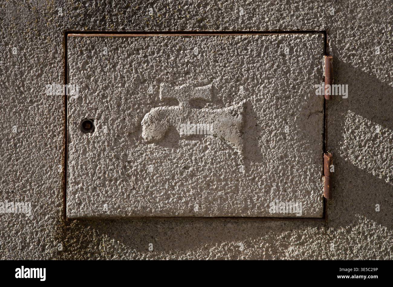 Sportello del contatore d'acqua nascosto nella parete esterna di una casa. Simbolo del rubinetto domestico in rilievo Foto Stock
