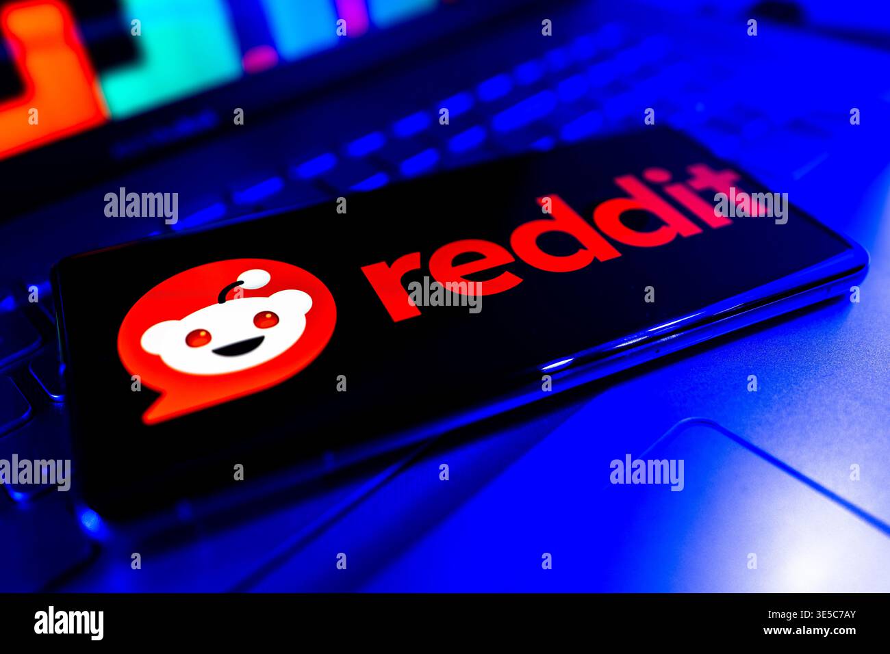 Logo Reddit visualizzato sullo schermo con sfondo del grafico del mercato finanziario che rappresenta le tendenze dei social media e del mercato azionario Foto Stock