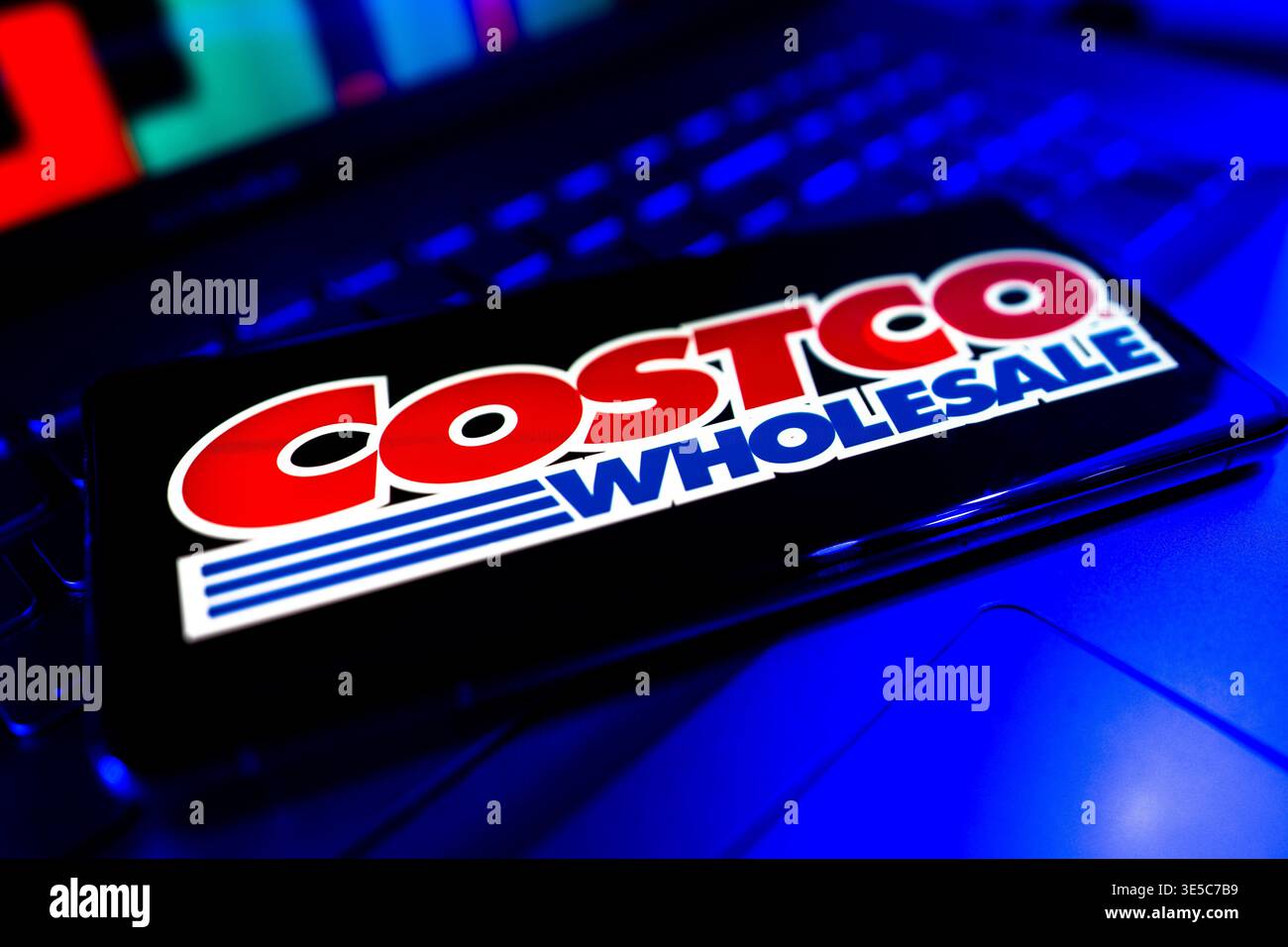 Logo Costco all'ingrosso visualizzato sullo schermo con sfondo grafico del mercato finanziario che rappresenta le prestazioni delle scorte al dettaglio e le tendenze economiche Foto Stock