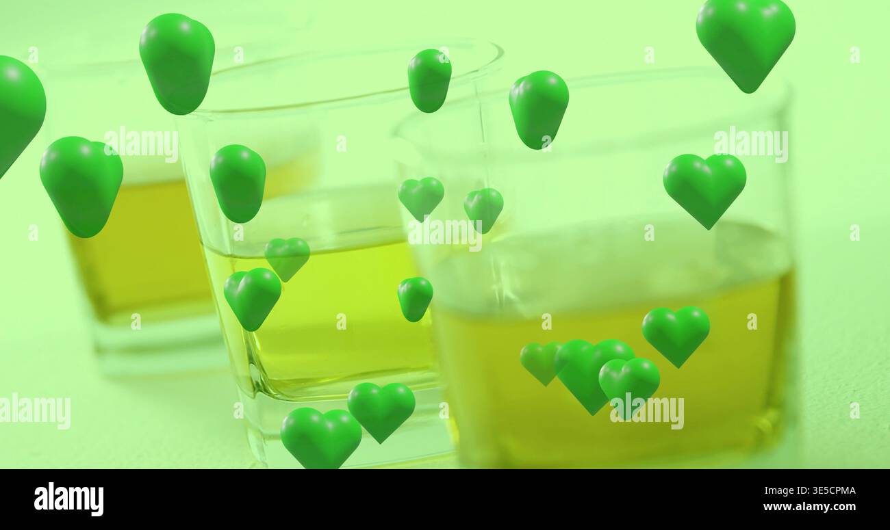 Visualizzazione di tre bicchieri quadrati di vetro che trattengono il liquido ambrato sul tavolo da studio, con cuori verdi Foto Stock