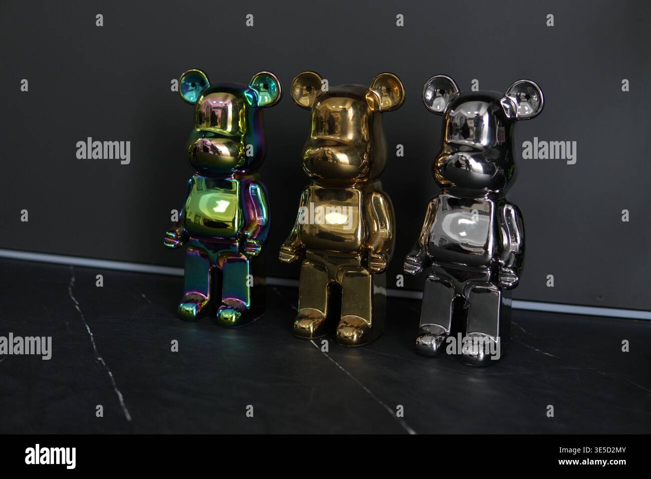 Tre statuette a orso metallizzate con superfici lucide riflettenti in cromo, oro e finitura iridescente visualizzate su sfondo scuro. Design moderno Foto Stock