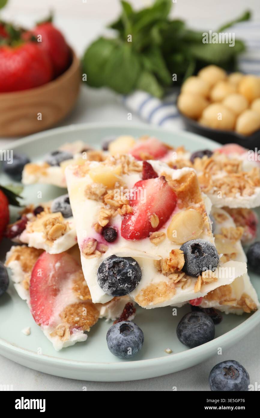 Pezzi di gustosa corteccia di yogurt con frutti di bosco e muesli sul tavolo leggero, primo piano Foto Stock