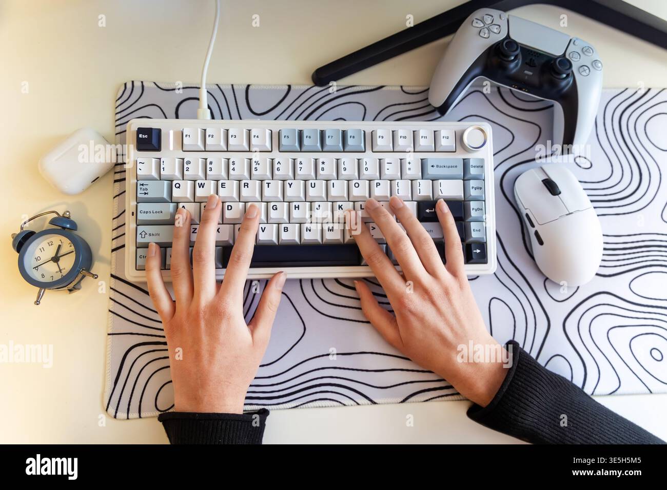 Digitazione manuale sulla moderna configurazione di Gaming Desk. Vista dall'alto della tastiera compatta accanto al mouse, al controller di gioco, all'orologio e alla custodia degli auricolari di Foto Stock