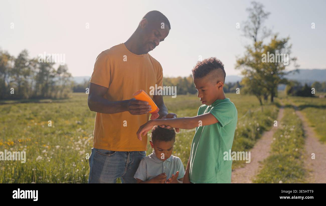 Mentre trascorreva del tempo all'aperto in estate, un padre applicava la crema solare ai suoi figli per tenerli al sicuro dal sole. Foto Stock