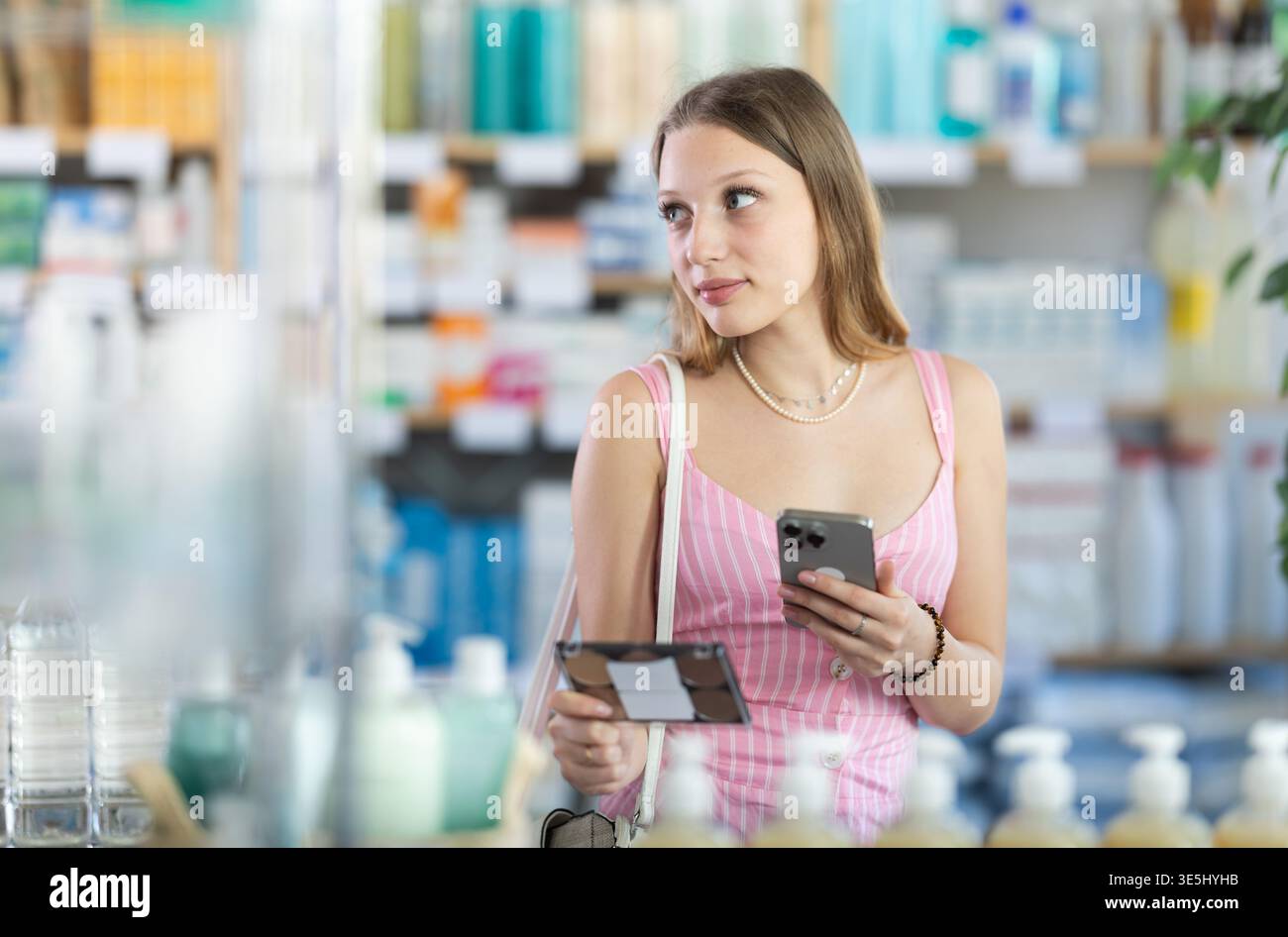 Ragazza in abiti estivi scansiona il codice sui cosmetici per controllare la data di scadenza Foto Stock