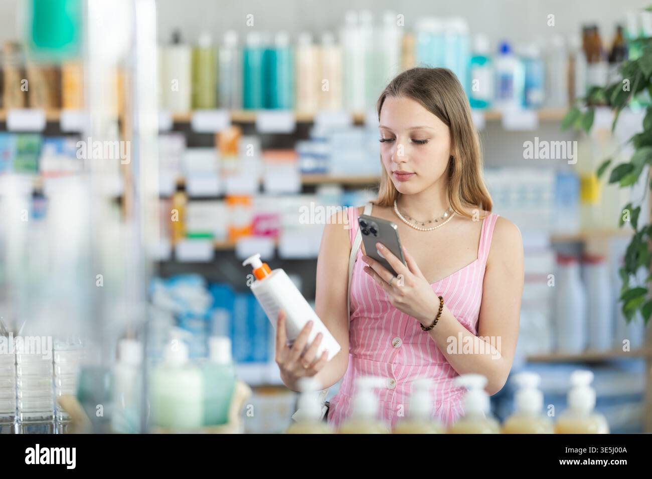 Ragazza in abiti estivi scansiona il codice sulla confezione della crema per controllare la data di scadenza Foto Stock