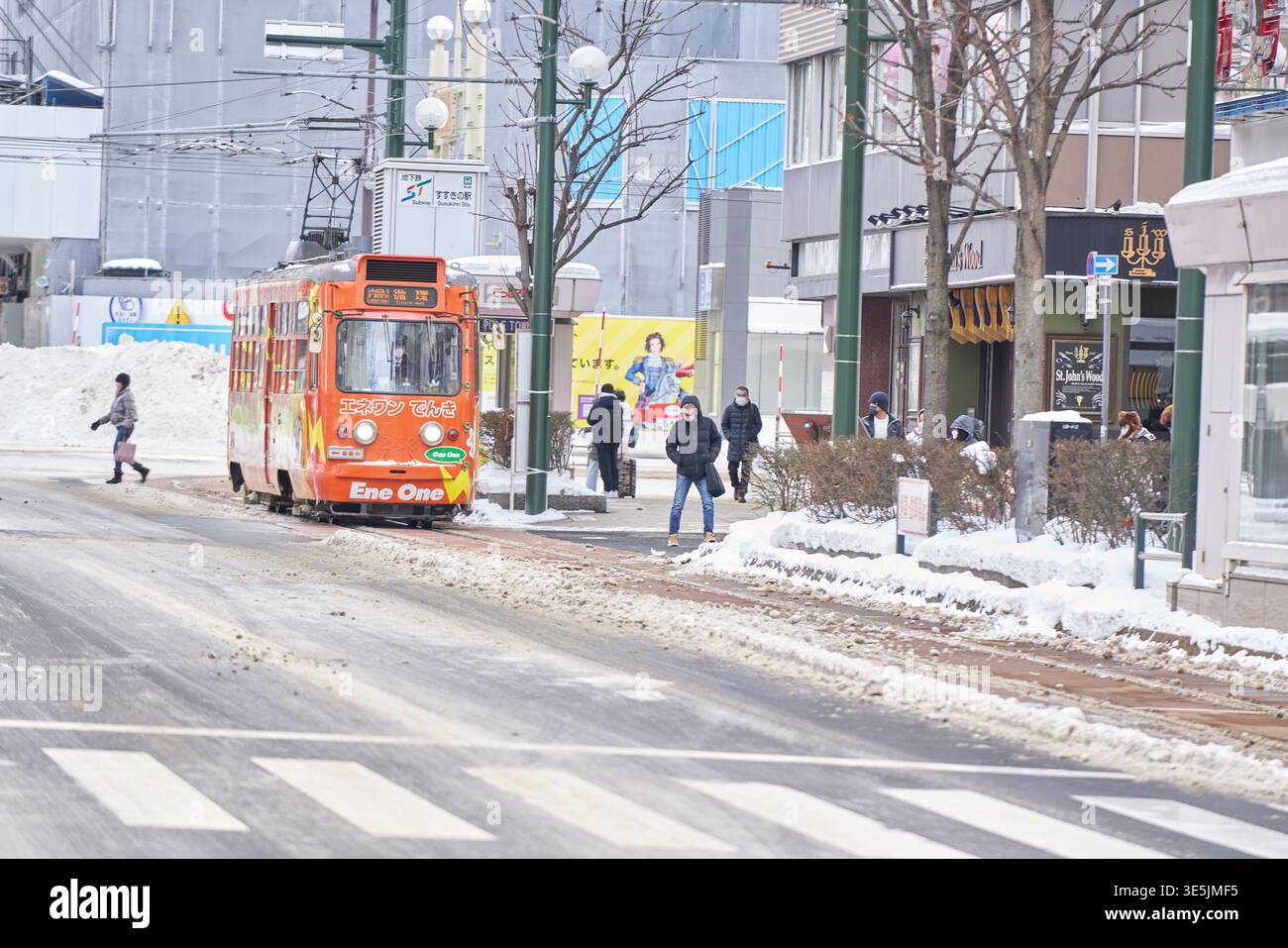 Una pittoresca scena stradale invernale a Sapporo, Hokkaido. Un tram d'epoca arancione corre lungo le piste innevate, creando un m nostalgico e romantico Foto Stock