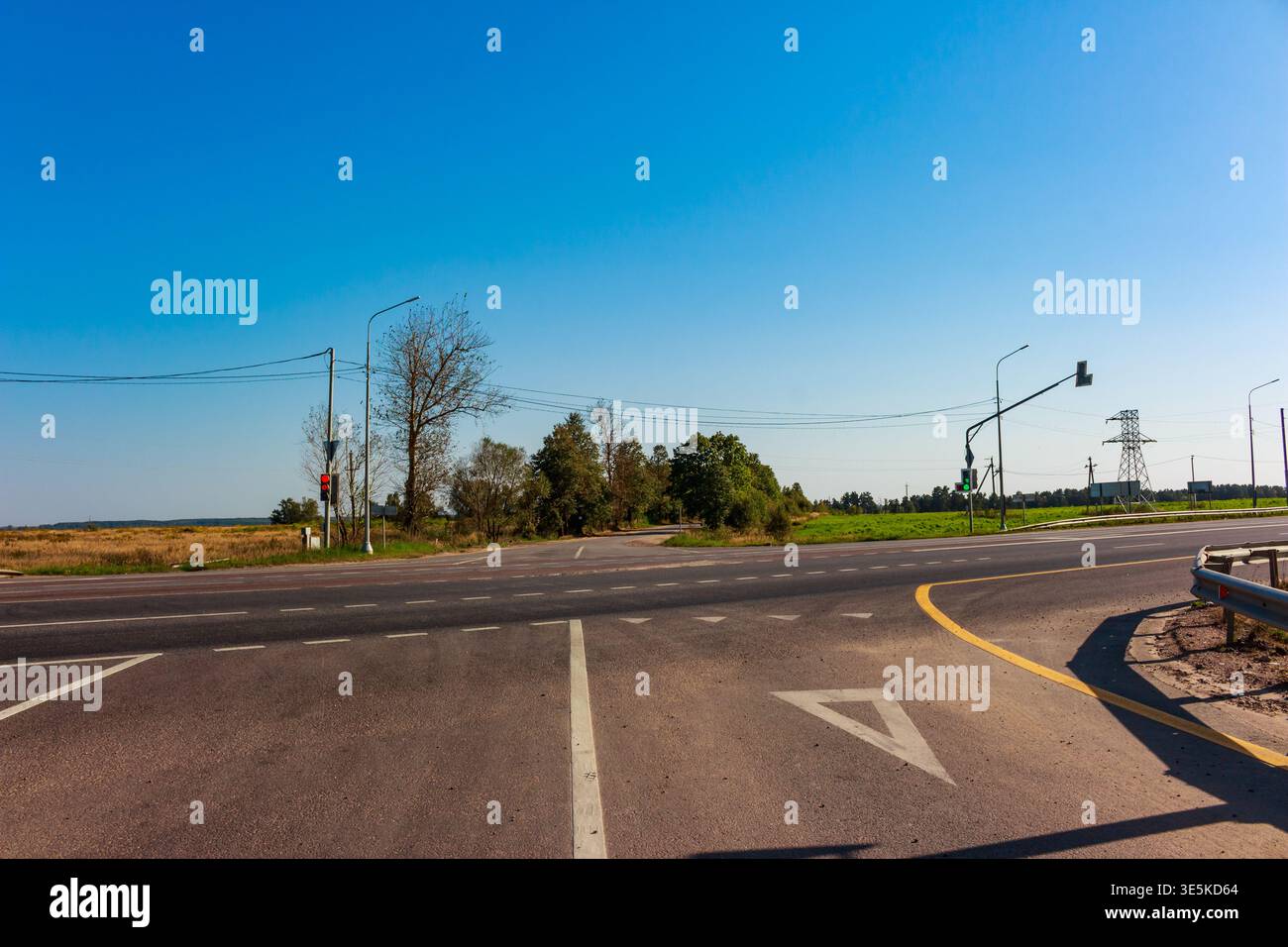 Incrocio stradale rurale sotto un vasto cielo azzurro, con segnali stradali e linee elettriche in mezzo a fogliame secco e verde che segnalano i viaggi verso la fine dell'estate Foto Stock