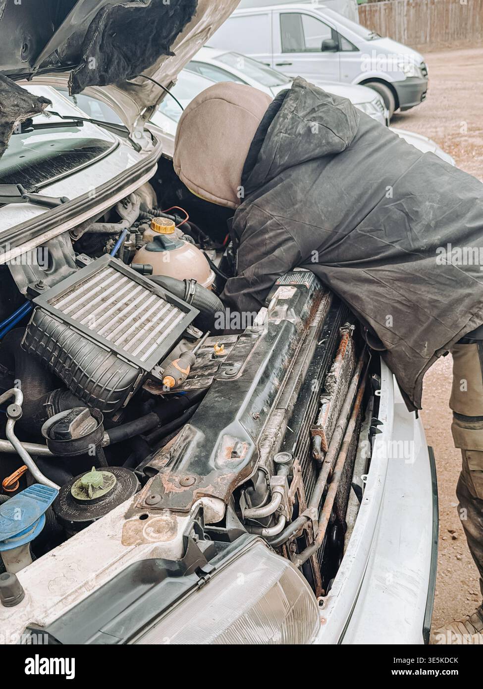 Riga, Lettonia - 31 marzo 2026: Tecnico che ispeziona e ripara il motore di un'auto sotto un cofano aperto in un ambiente all'aperto. Concetto di manutenzione del veicolo Foto Stock