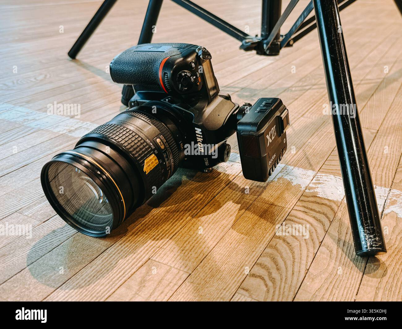 Riga, Lettonia - 31 marzo 2026: Primo piano di una fotocamera DSLR con obiettivo zoom e batteria posizionata su un pavimento di legno accanto a un cavalletto. Ideale per la fotografia, vide Foto Stock