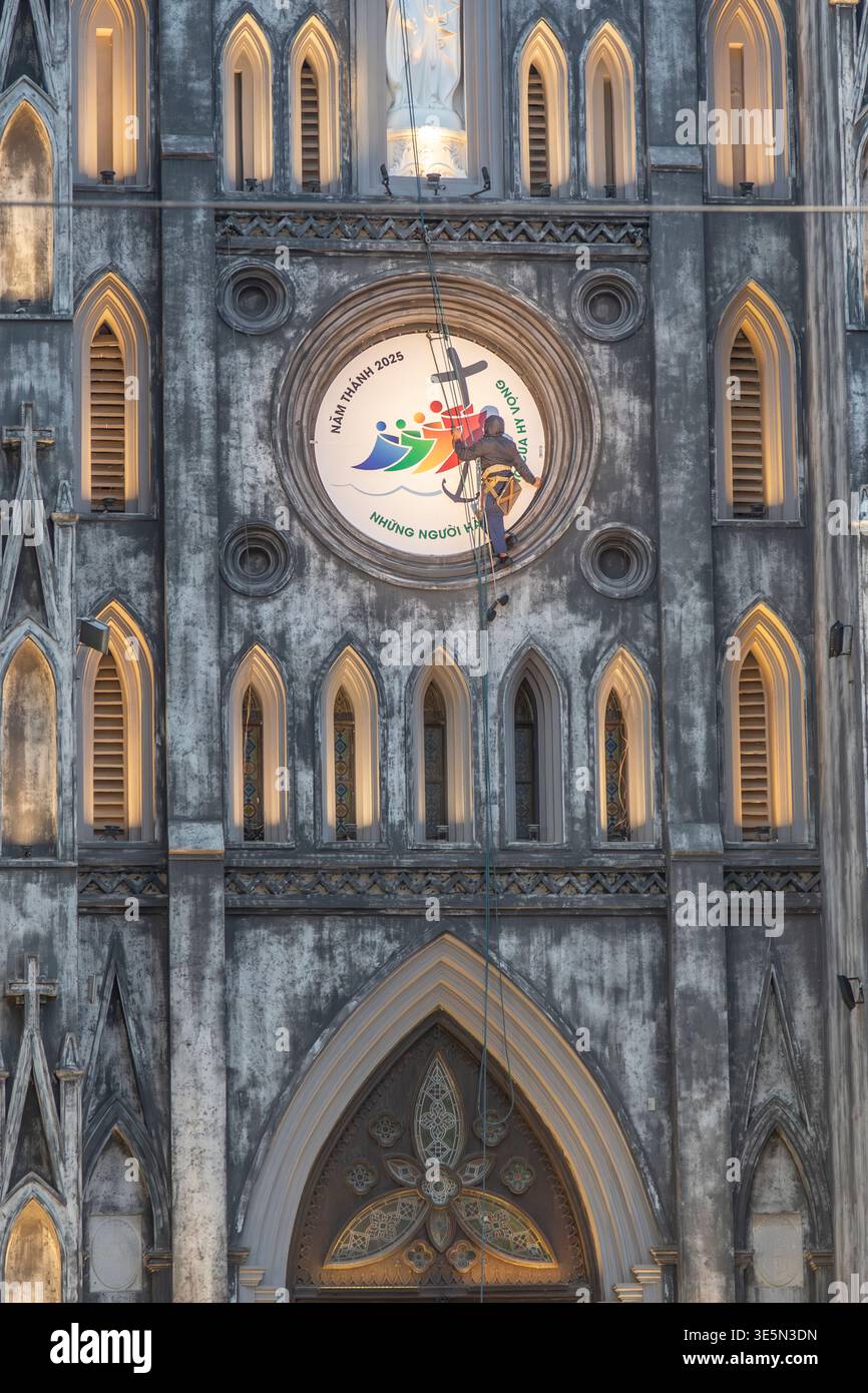 Un operaio che si arrampica sulla faccia della Cattedrale di San Giuseppe, Hanoi, Vietnam. Foto Stock